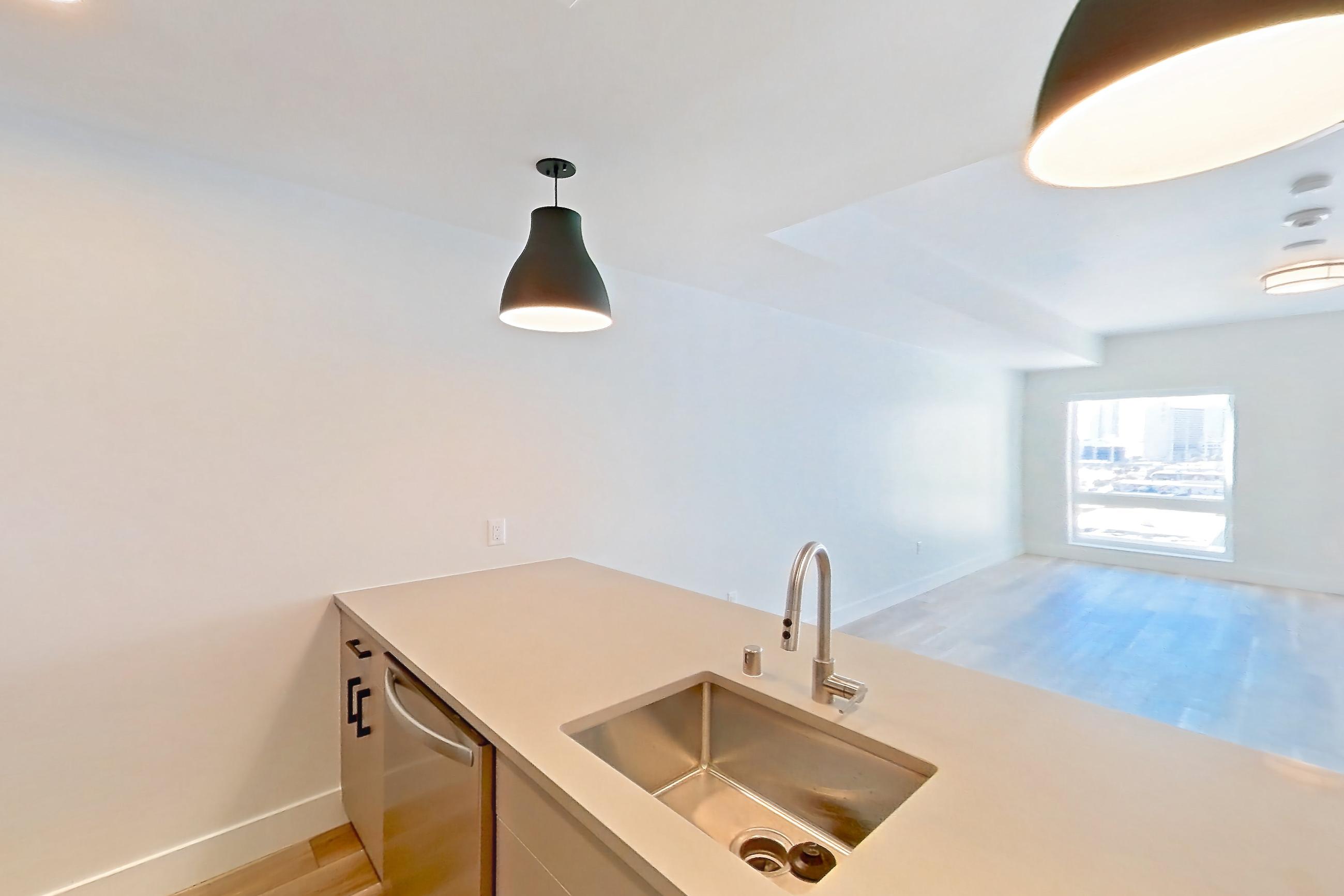 Kitchen with gas range, kitchen island, light countertops, light wood-finish flooring, oven/range, refrigerator, and stainless steel appliances, Apartment 711 at The Myles