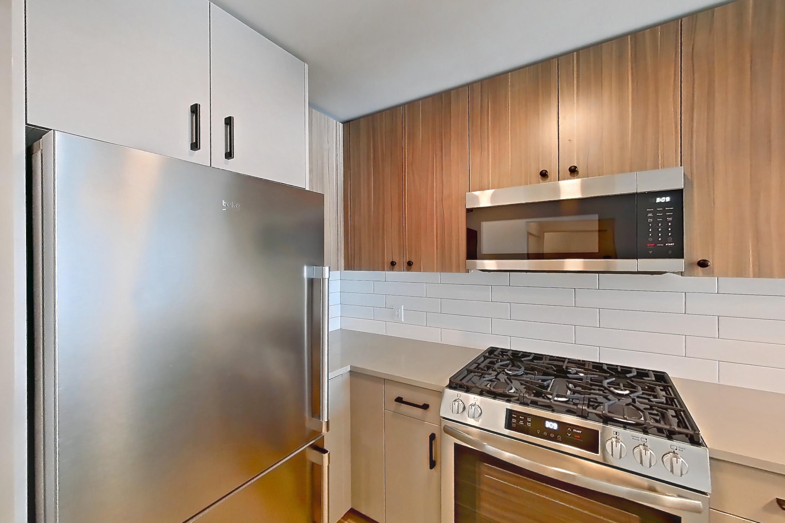 Kitchen with dishwasher, gas range, light countertops, light wood-finish flooring, oven/range, refrigerator, and stainless steel appliances, Apartment 712 at The Myles