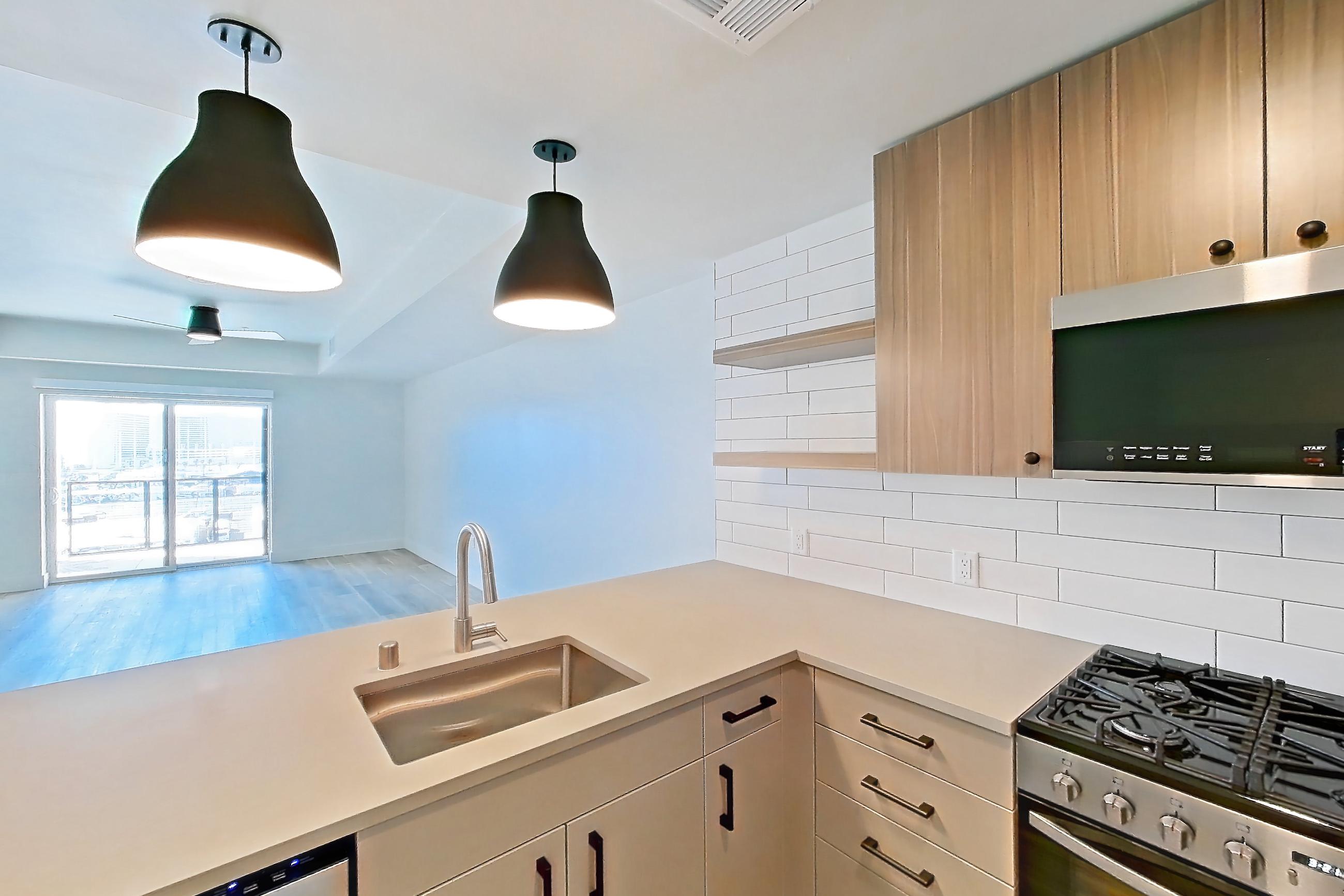 Kitchen with dishwasher, gas range, light countertops, light wood-finish flooring, oven/range, refrigerator, and stainless steel appliances, Apartment 713 at The Myles