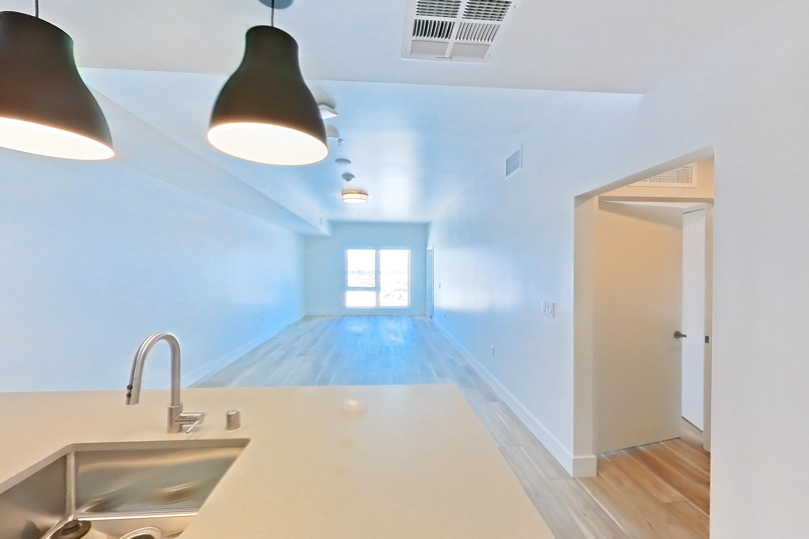 Kitchen with dishwasher, gas range, light countertops, light stone countertops, light wood-finish flooring, oven/range, refrigerator, and stainless steel appliances, Apartment 714 at The Myles