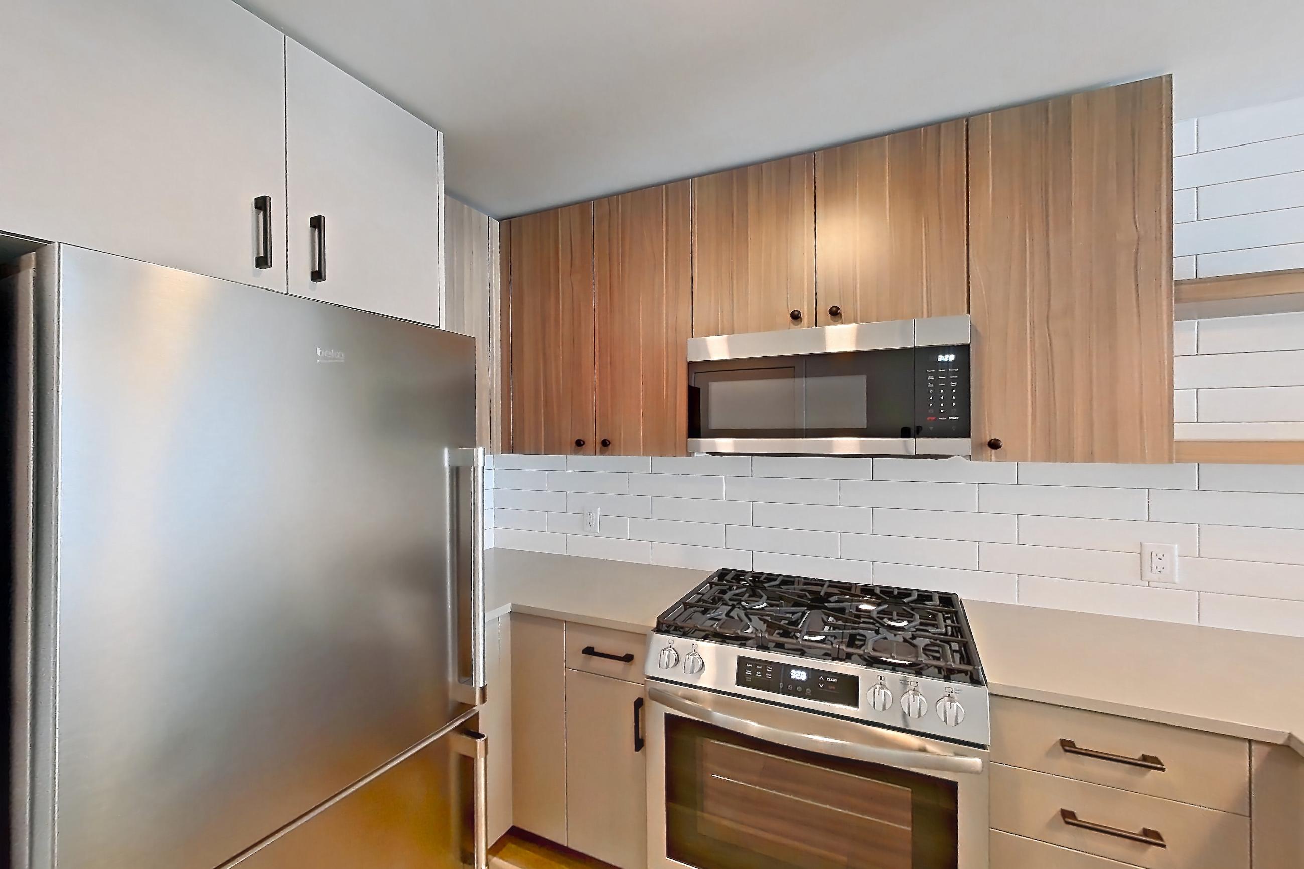 Kitchen with dishwasher, gas range, light countertops, light stone countertops, light wood-finish flooring, oven/range, refrigerator, and stainless steel appliances, Apartment 714 at The Myles
