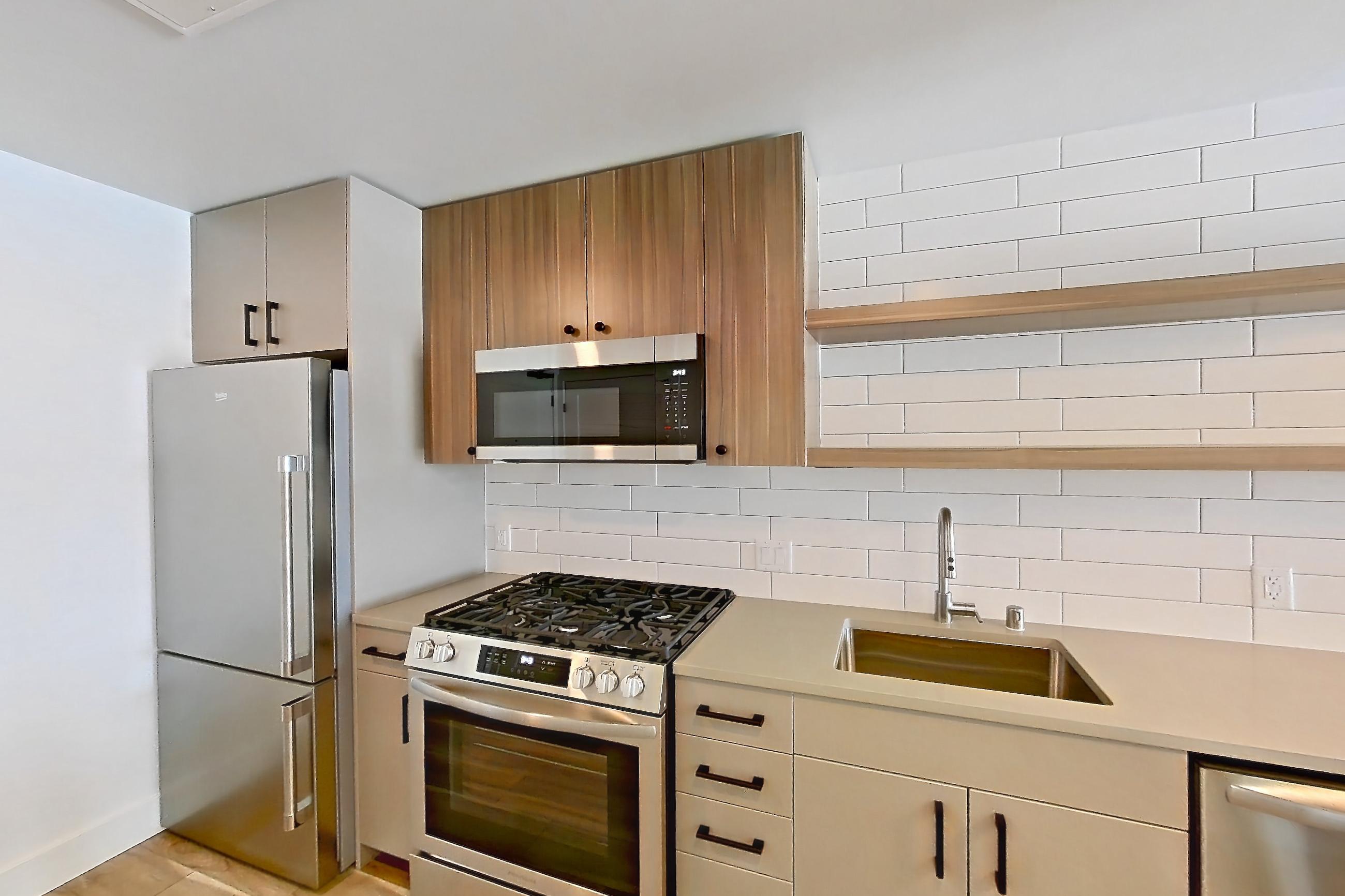 Kitchen with dishwasher, gas range, light countertops, light wood-finish flooring, microwave, oven/range, refrigerator, and stainless steel appliances, Apartment 716 at The Myles