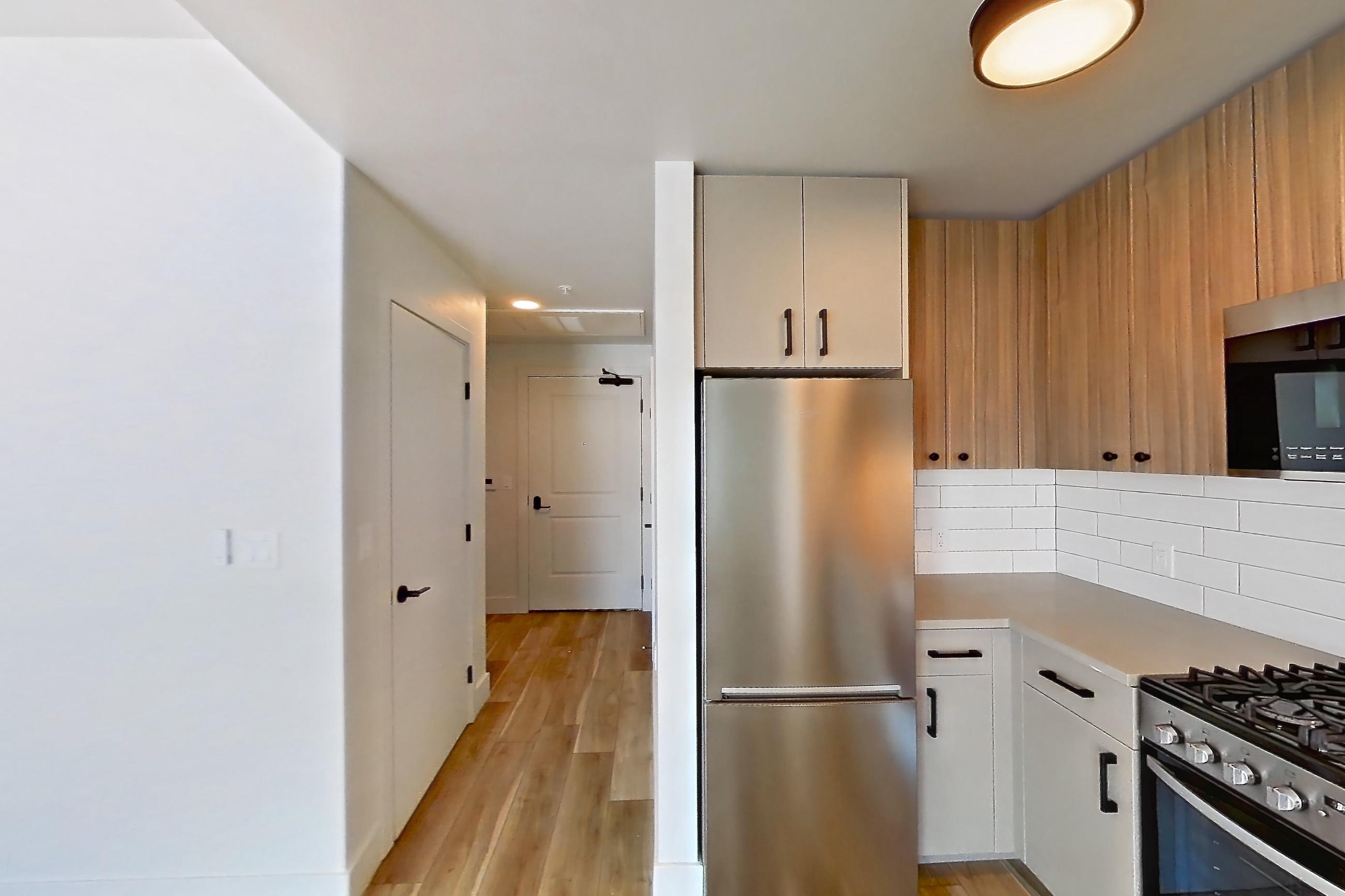 Kitchen with gas range, light countertops, light wood-finish flooring, oven/range, refrigerator, and stainless steel appliances, Apartment 718 at The Myles