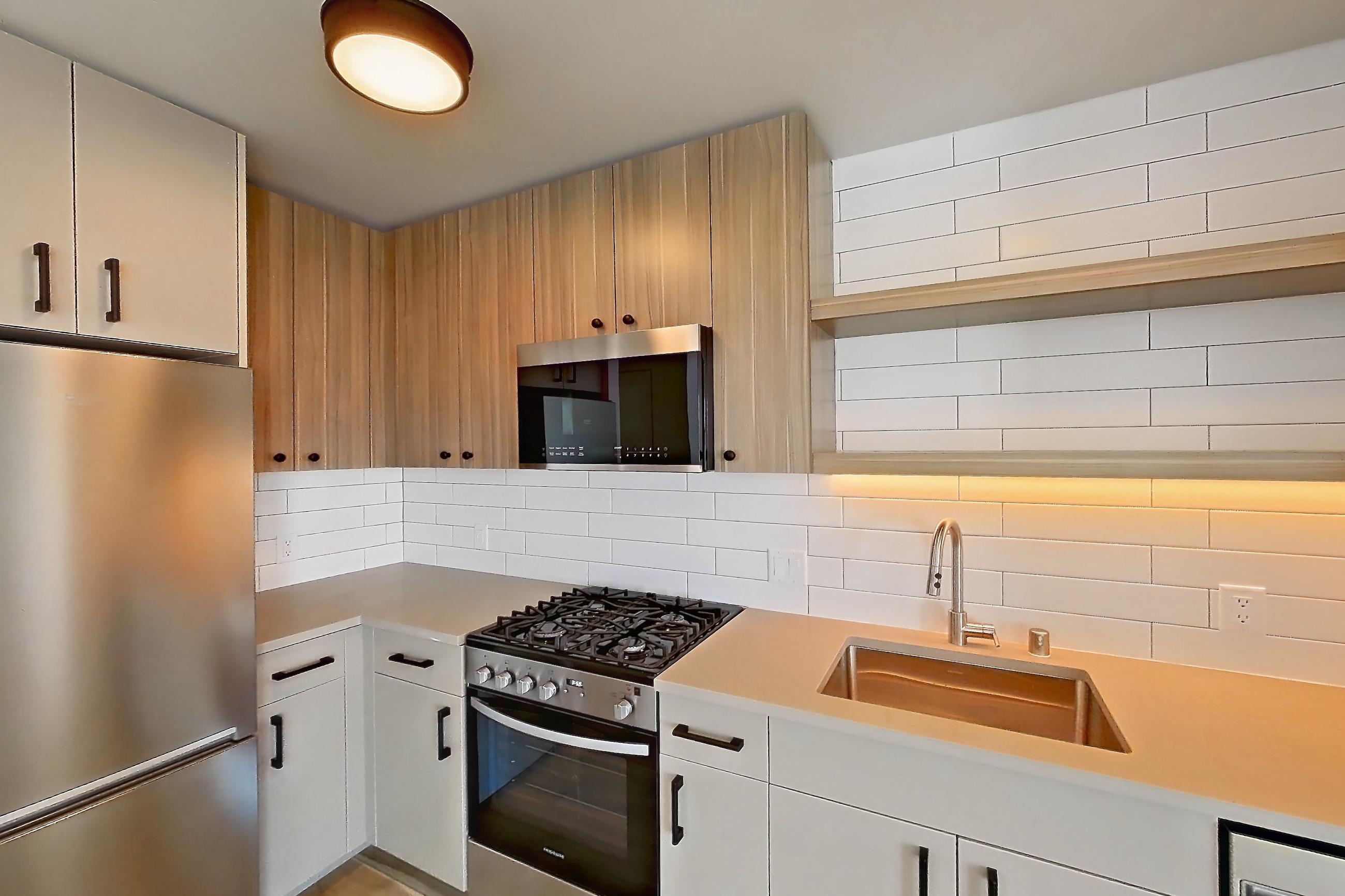Kitchen with gas range, light countertops, light wood-finish flooring, oven/range, refrigerator, and stainless steel appliances, Apartment 718 at The Myles
