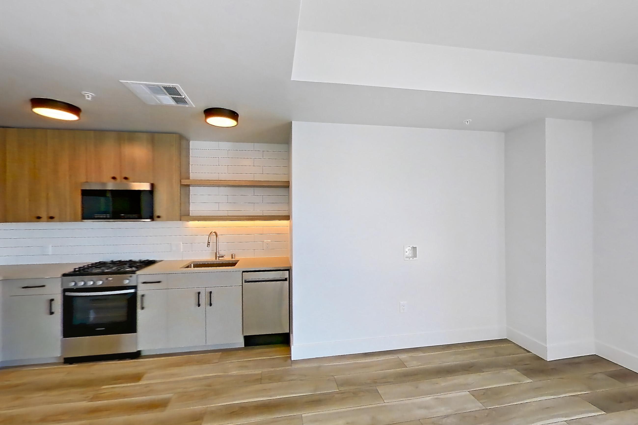 Living space with dishwasher, gas range, light countertops, light wood-finish flooring, oven/range, refrigerator, and stainless steel appliances, Apartment 718 at The Myles