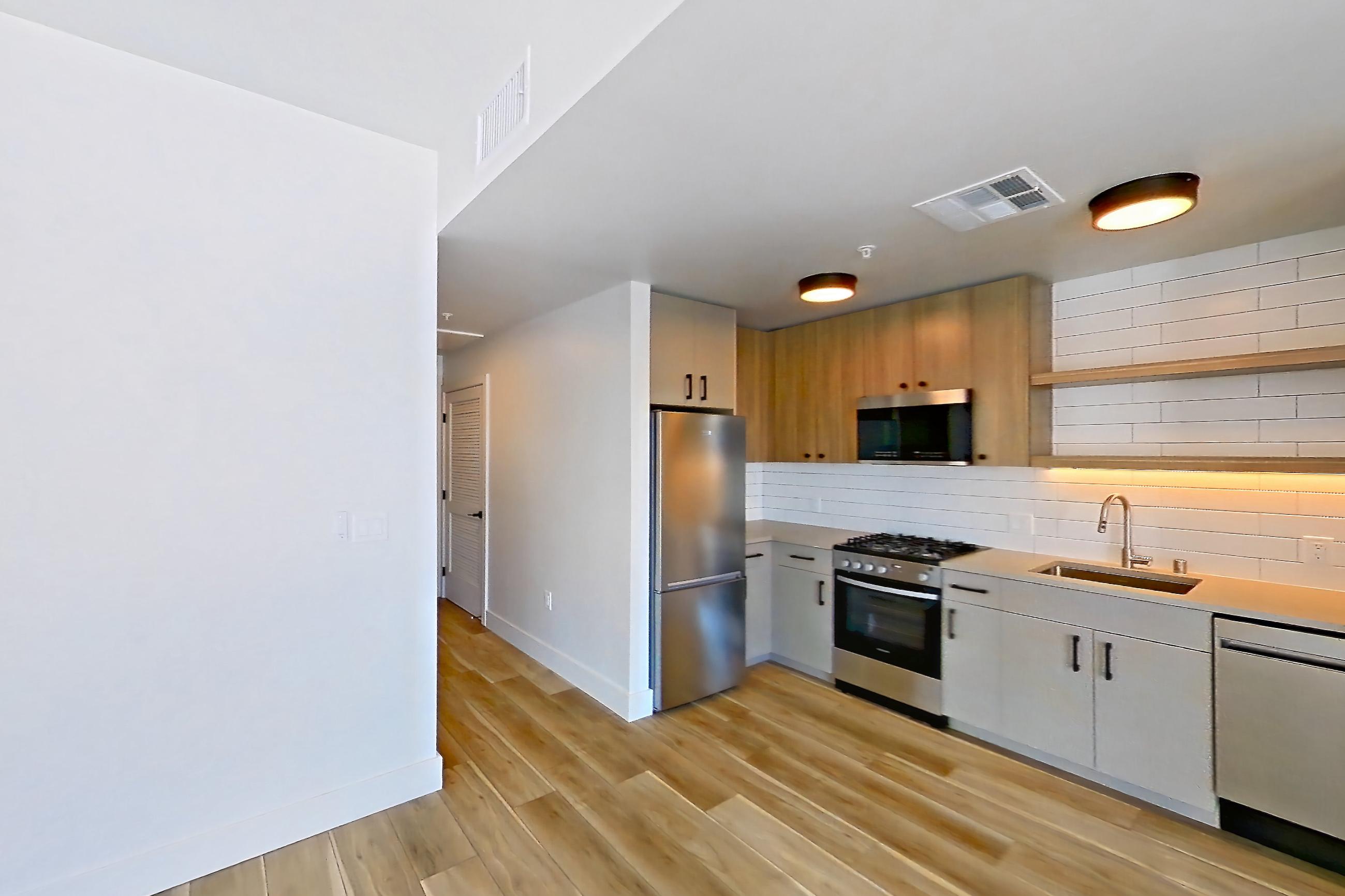 Living space with dishwasher, gas range, light countertops, light wood-finish flooring, oven/range, refrigerator, and stainless steel appliances, Apartment 718 at The Myles