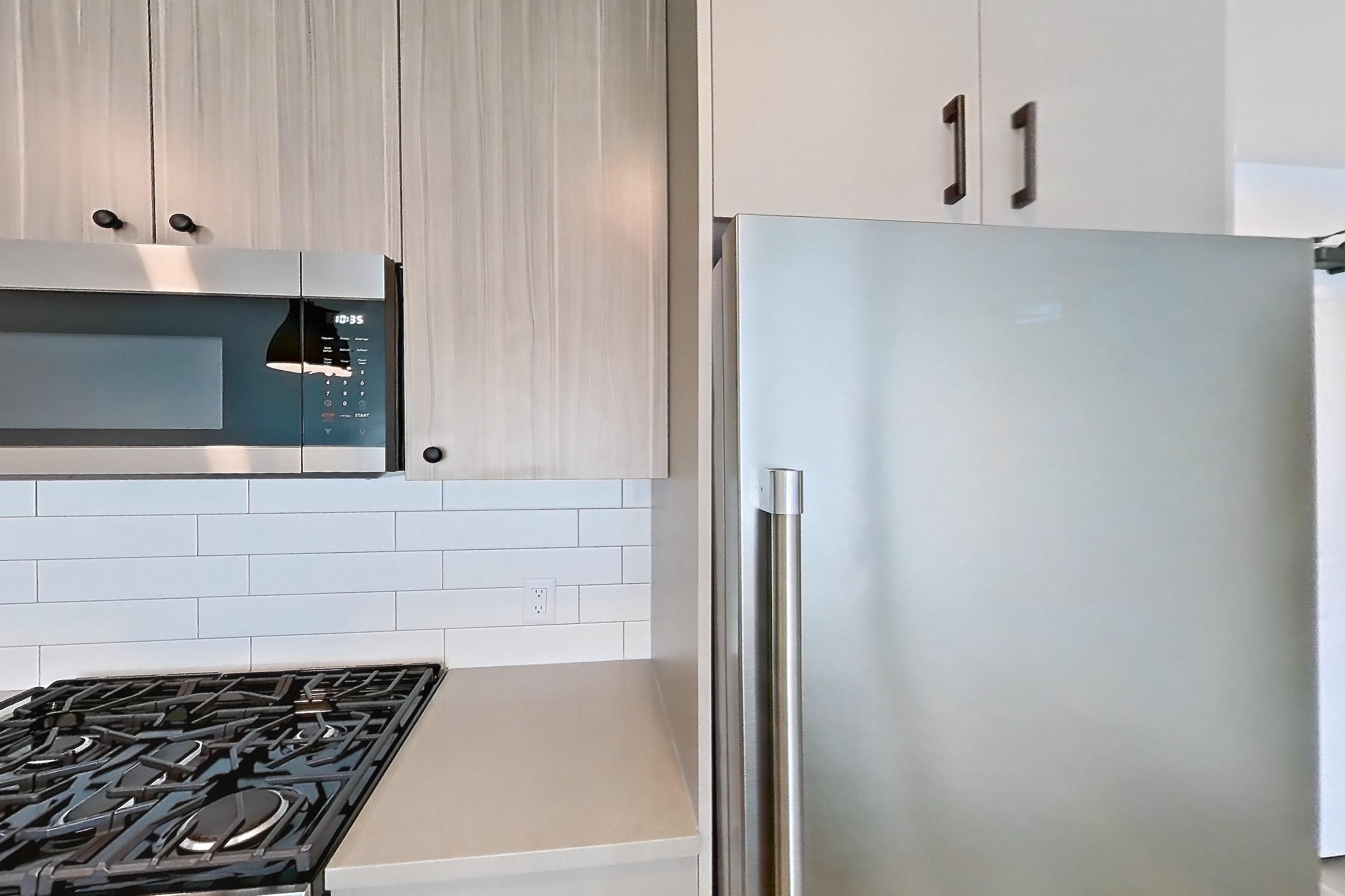 Kitchen with dishwasher, gas range, light countertops, light wood-finish flooring, oven/range, refrigerator, and stainless steel appliances, Apartment 721 at The Myles