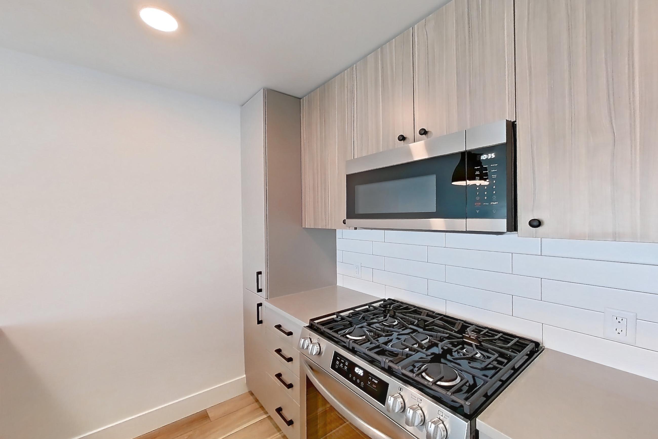 Kitchen with dishwasher, gas range, light countertops, light wood-finish flooring, oven/range, refrigerator, and stainless steel appliances, Apartment 721 at The Myles