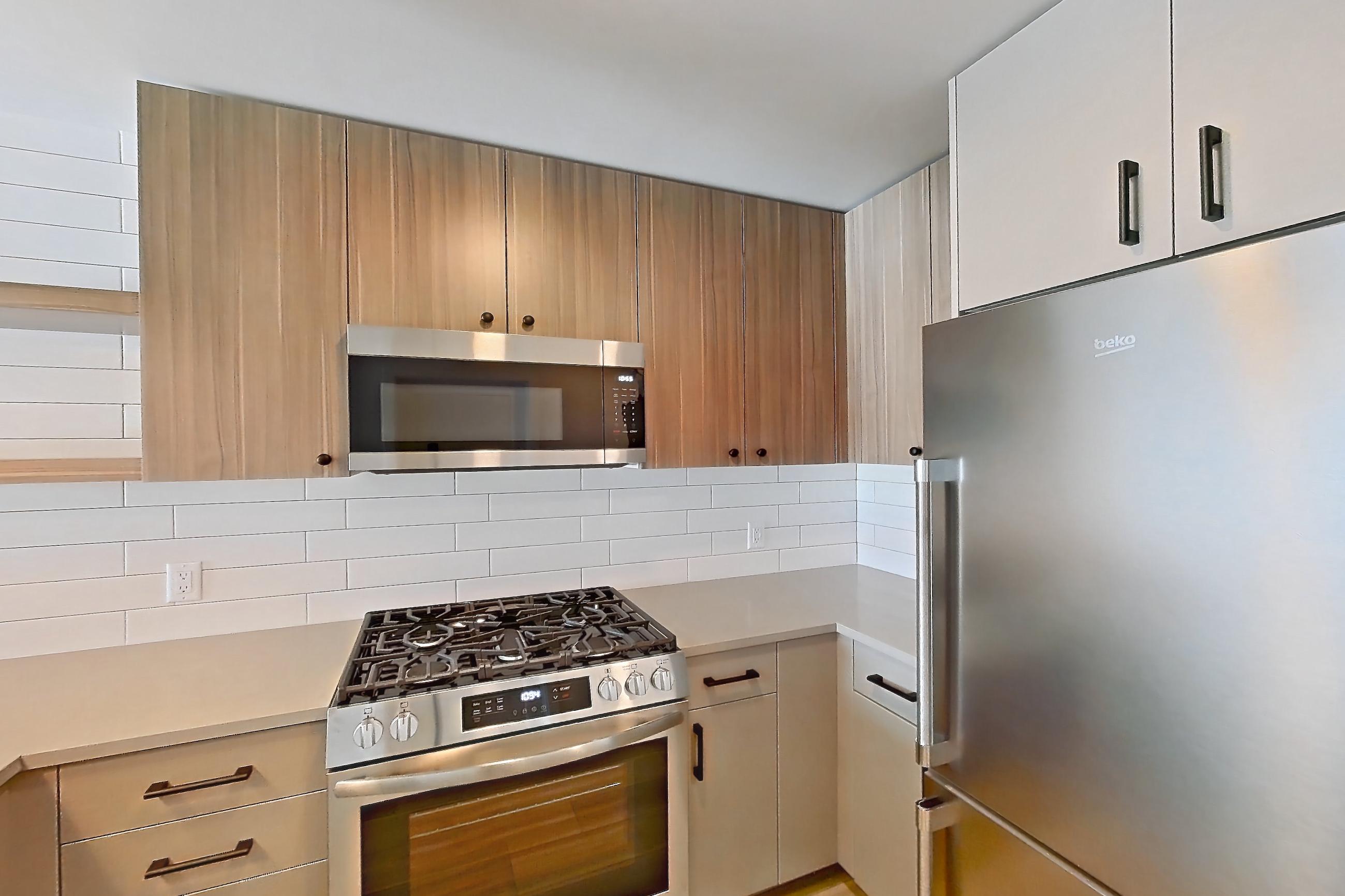 Kitchen with dishwasher, gas range, light countertops, light wood-finish flooring, microwave, oven/range, refrigerator, and stainless steel appliances, Apartment 722 at The Myles