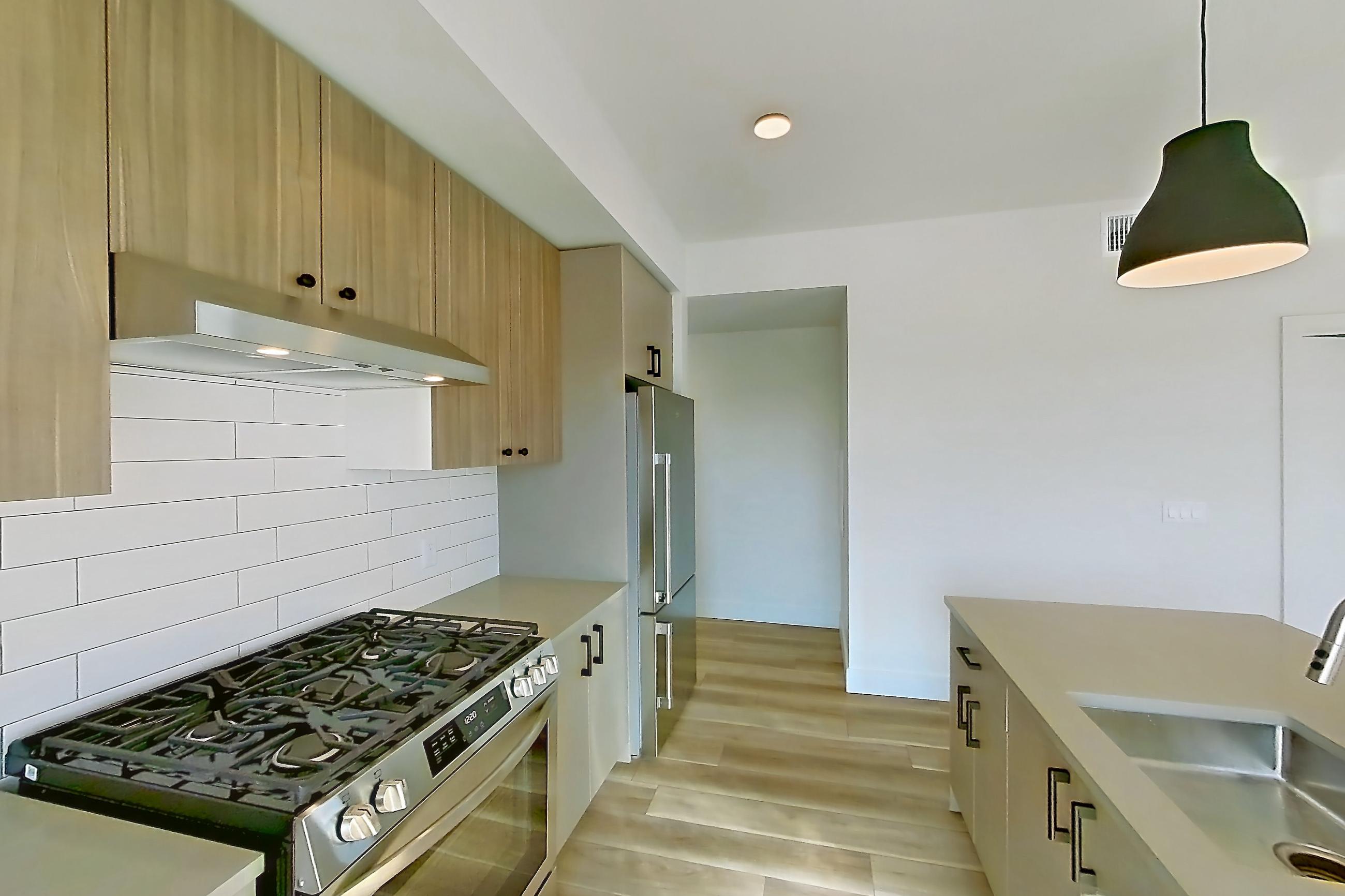 Kitchen with gas range, kitchen island, light countertops, light wood-finish flooring, oven/range, range hood, refrigerator, and stainless steel appliances, Apartment 724 at The Myles