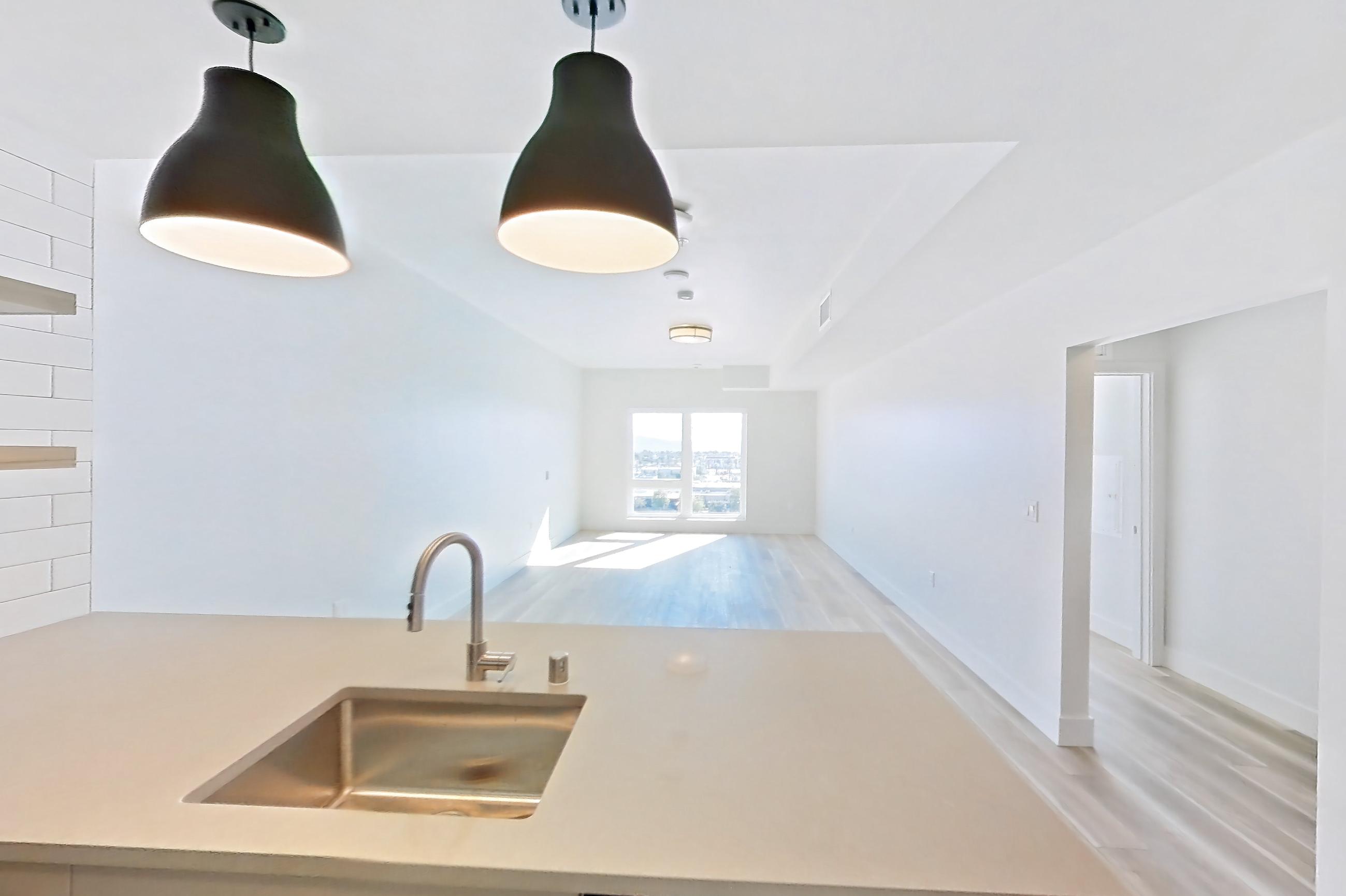 Kitchen with dishwasher, gas range, light countertops, light stone countertops, light wood-finish flooring, oven/range, refrigerator, and stainless steel appliances, Apartment 725 at The Myles