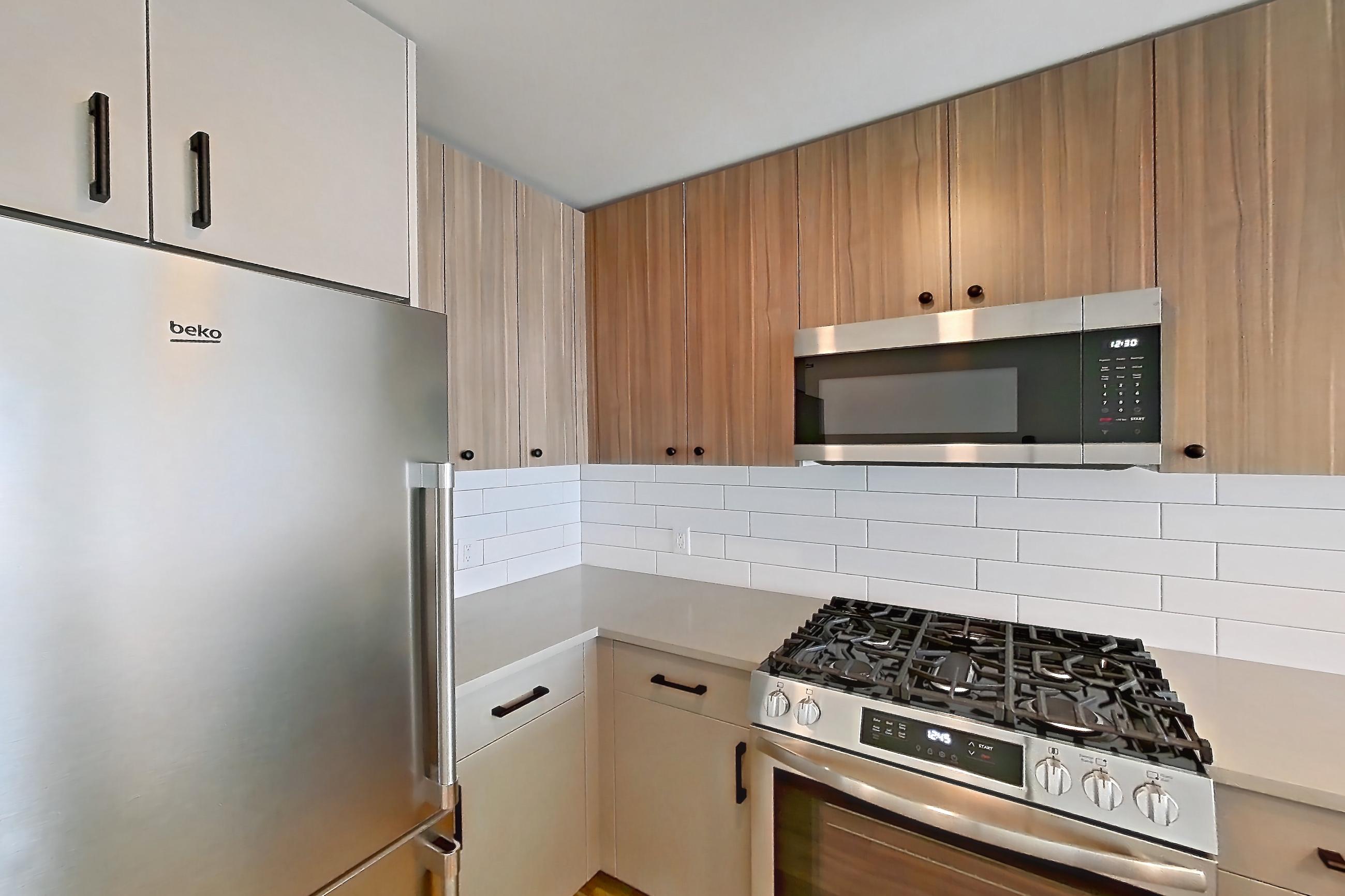 Kitchen with dishwasher, gas range, light countertops, light stone countertops, light wood-finish flooring, oven/range, refrigerator, and stainless steel appliances, Apartment 725 at The Myles