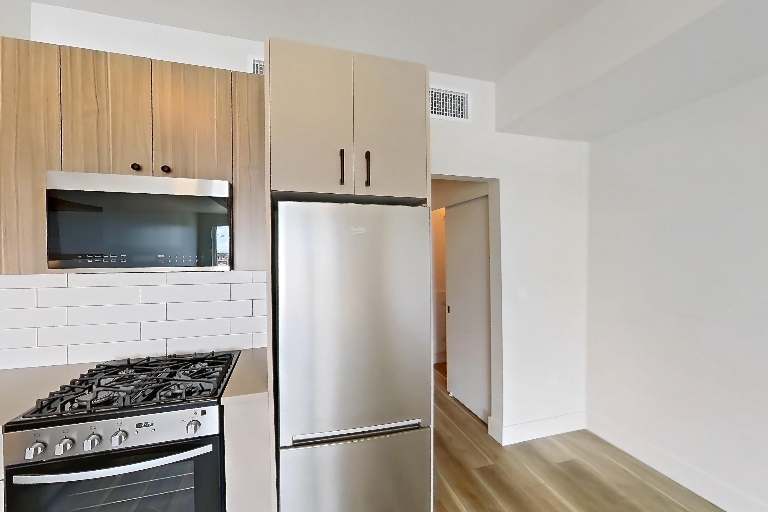 Kitchen with dishwasher, gas range, light countertops, light wood-finish flooring, oven/range, refrigerator, and stainless steel appliances, Apartment 726 at The Myles