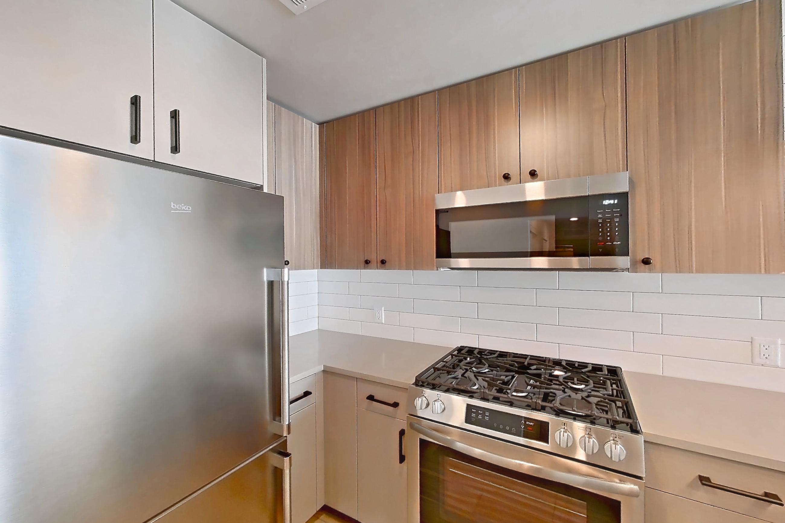 Kitchen with dishwasher, gas range, light countertops, light wood-finish flooring, oven/range, refrigerator, and stainless steel appliances, Apartment 727 at The Myles