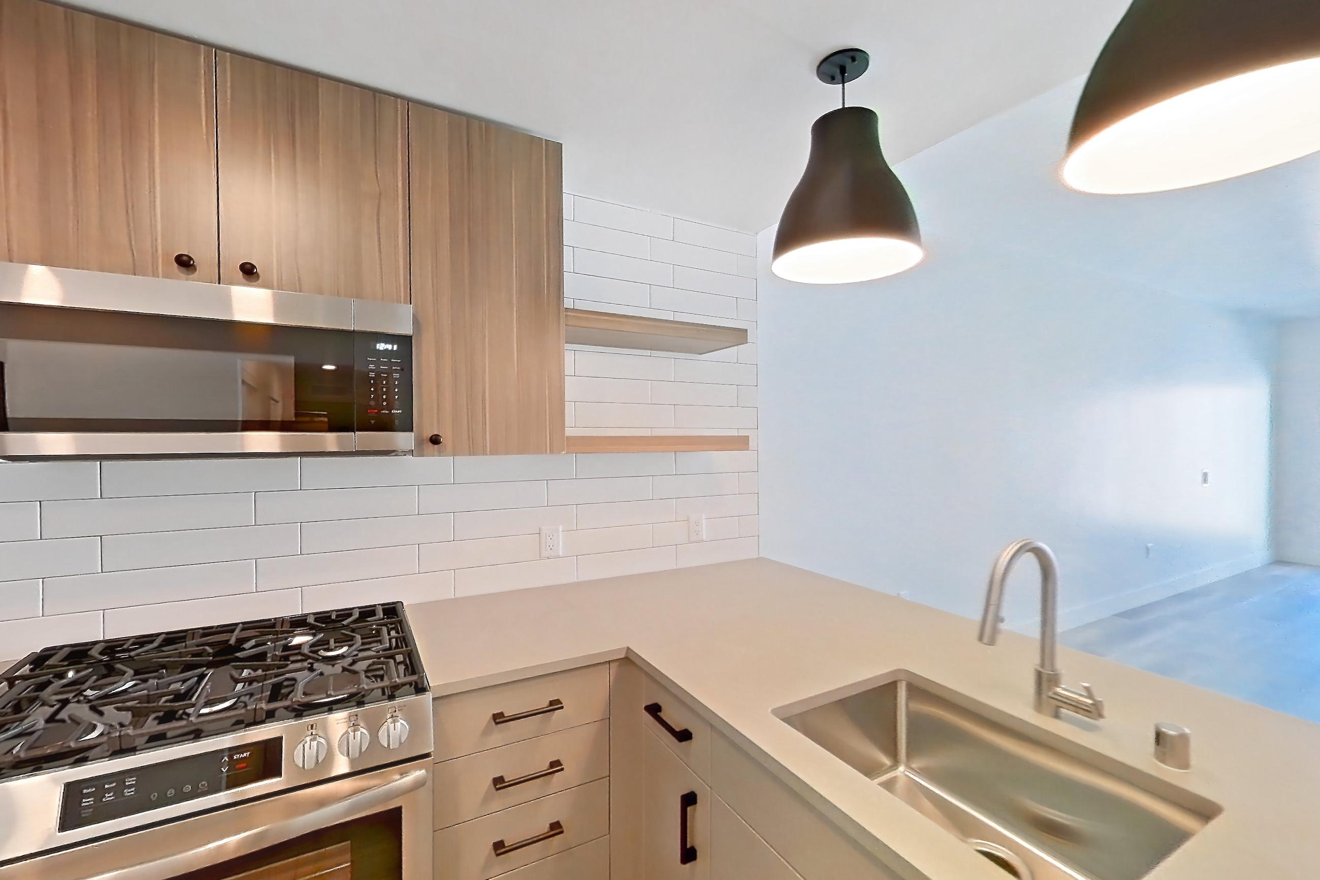 Kitchen with dishwasher, gas range, light countertops, light wood-finish flooring, oven/range, refrigerator, and stainless steel appliances, Apartment 727 at The Myles