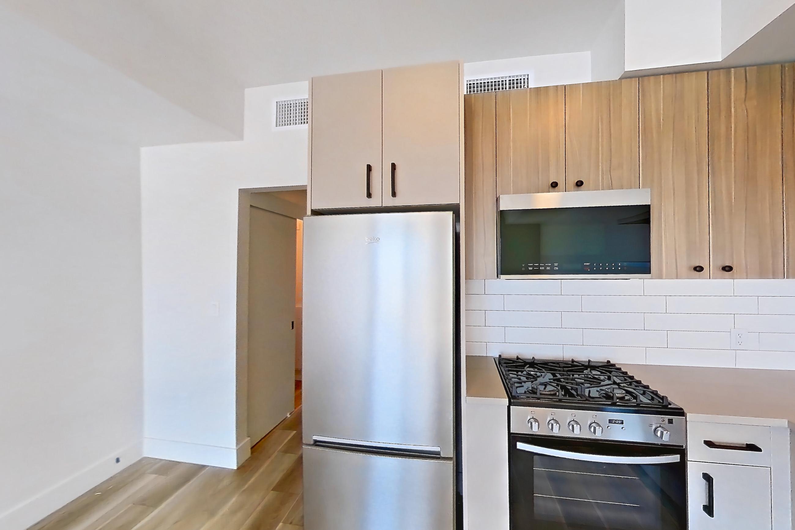 Kitchen with dishwasher, gas range, light countertops, light wood-finish flooring, oven/range, refrigerator, and stainless steel appliances, Apartment 728 at The Myles