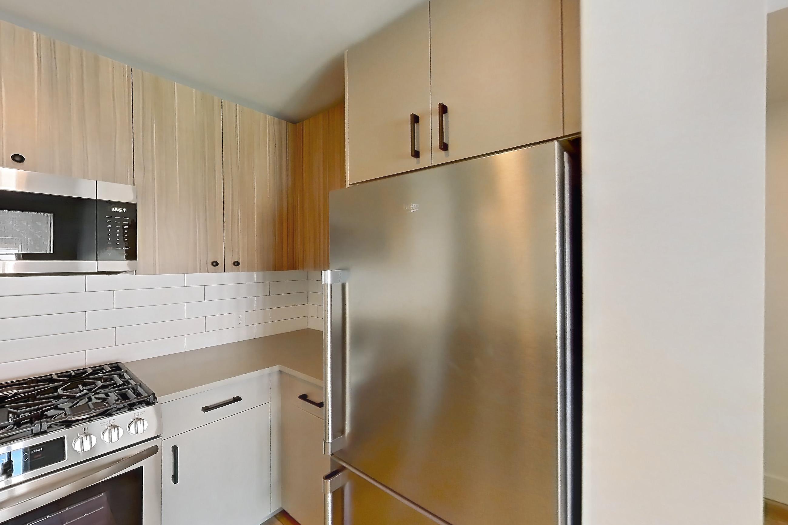 Kitchen with dishwasher, gas range, light countertops, light wood-finish flooring, microwave, oven/range, refrigerator, stainless steel appliances, and white appliances, Apartment 729 at The Myles