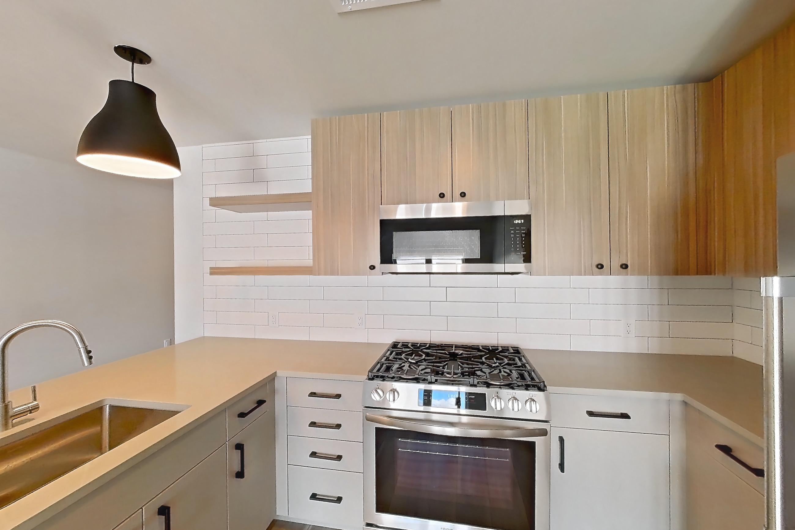 Kitchen with dishwasher, gas range, light countertops, light wood-finish flooring, microwave, oven/range, refrigerator, stainless steel appliances, and white appliances, Apartment 729 at The Myles