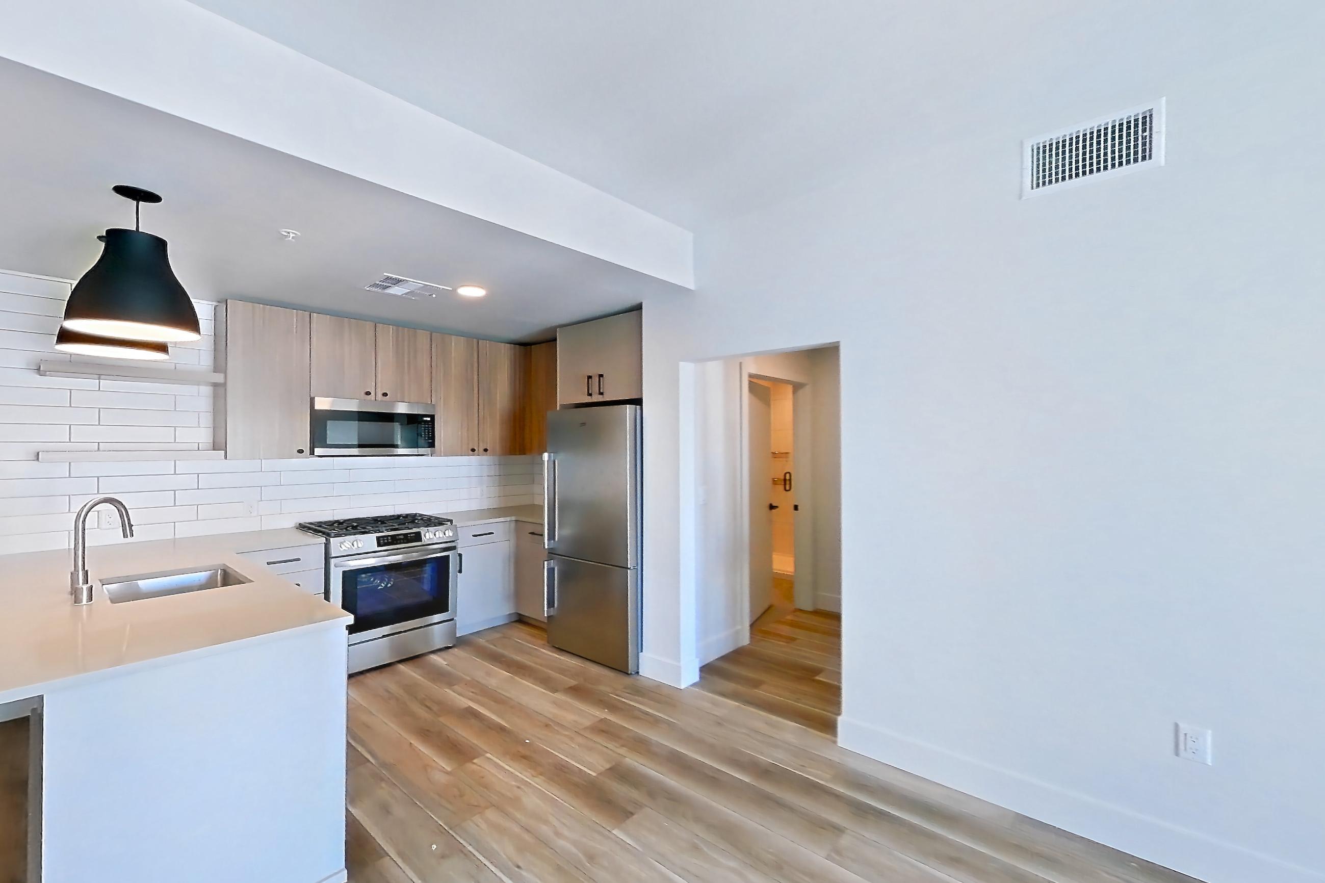 Living room with light countertops, light wood-finish flooring, refrigerator, and stainless steel appliances, Apartment 729 at The Myles