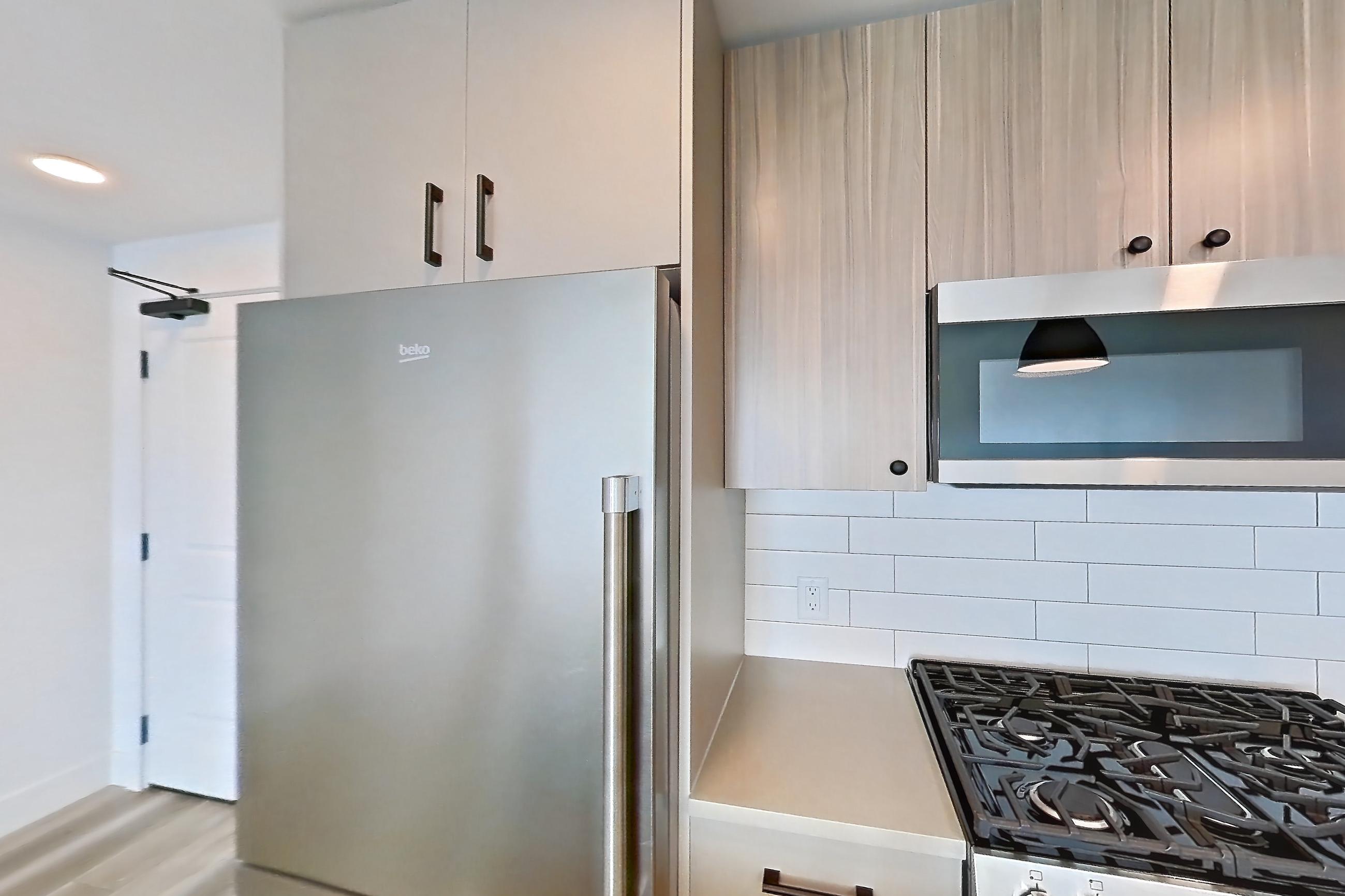 Kitchen with dishwasher, gas range, light countertops, light wood-finish flooring, oven/range, refrigerator, and stainless steel appliances, Apartment 730 at The Myles