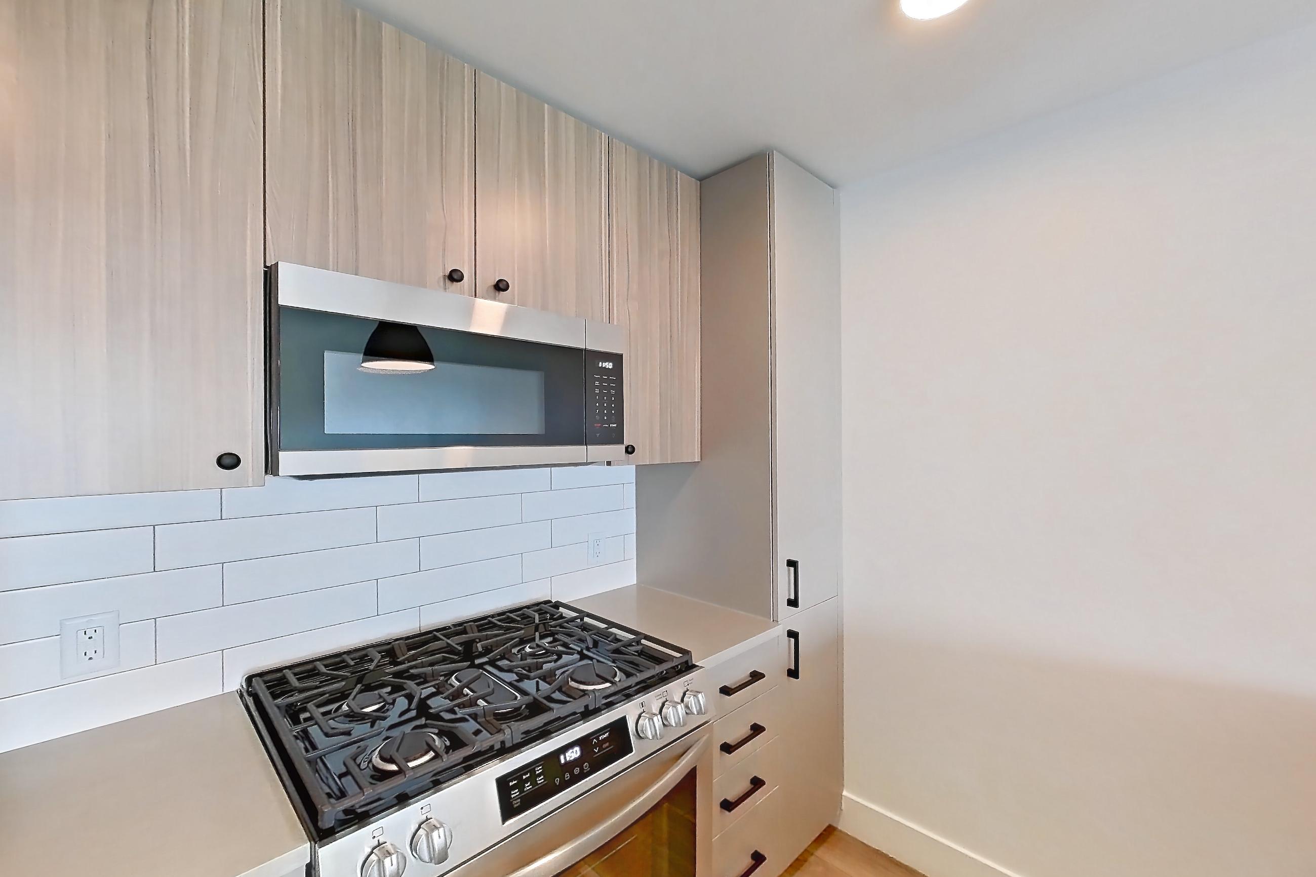 Kitchen with dishwasher, gas range, light countertops, light wood-finish flooring, oven/range, refrigerator, and stainless steel appliances, Apartment 730 at The Myles