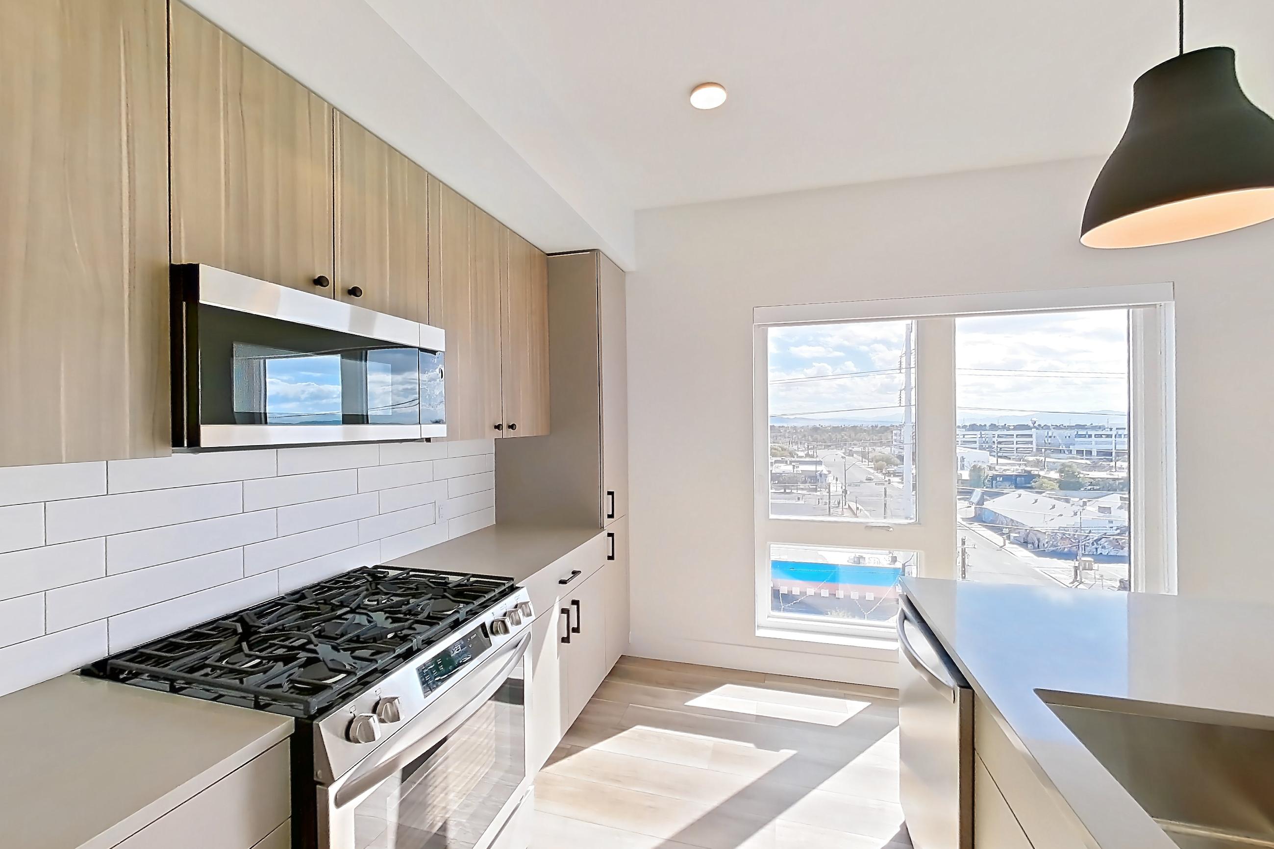 Kitchen with dishwasher, gas range, kitchen island, light countertops, light wood-finish flooring, oven/range, and stainless steel appliances, Apartment 731 at The Myles