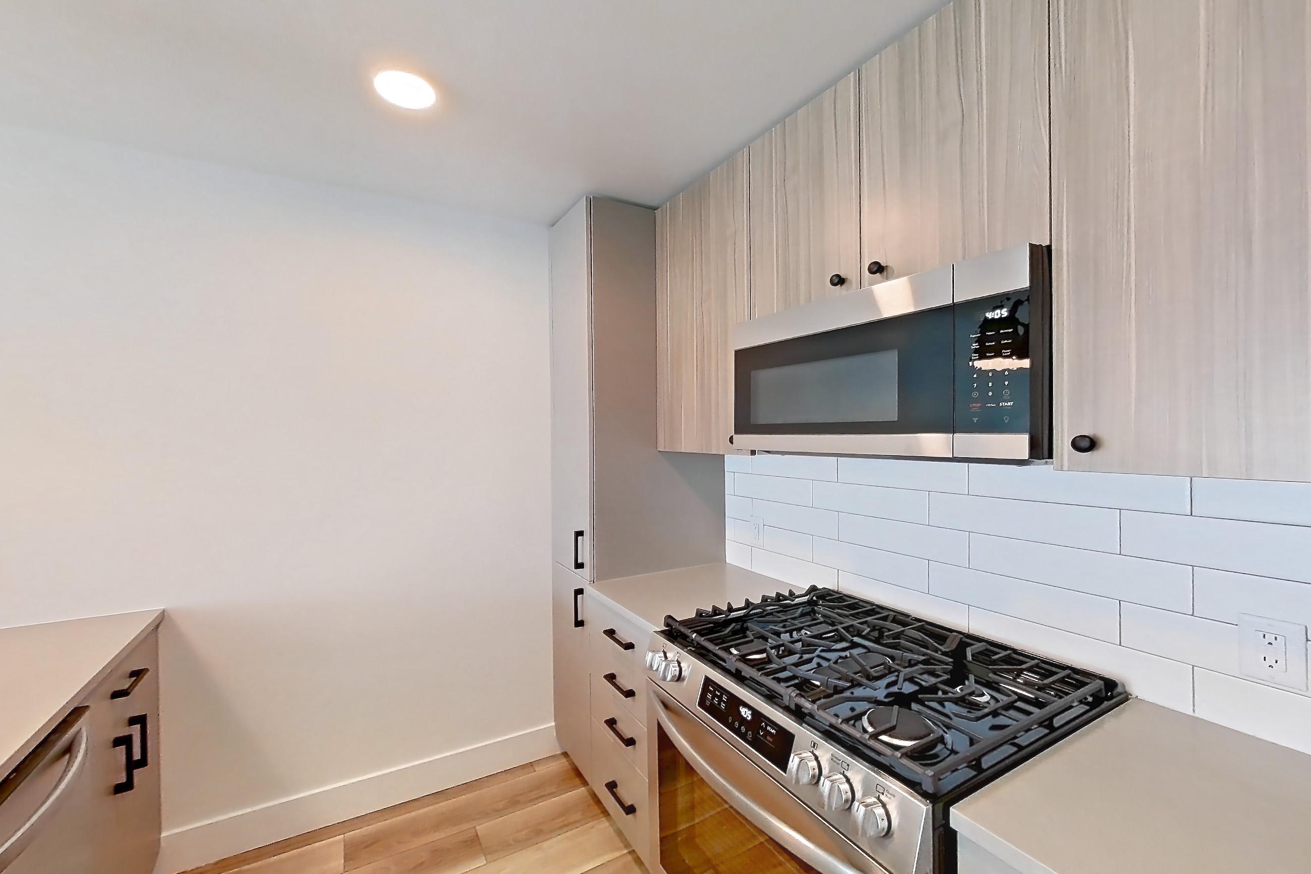 Kitchen with dishwasher, gas range, light countertops, light wood-finish flooring, oven/range, and stainless steel appliances, Apartment 736 at The Myles