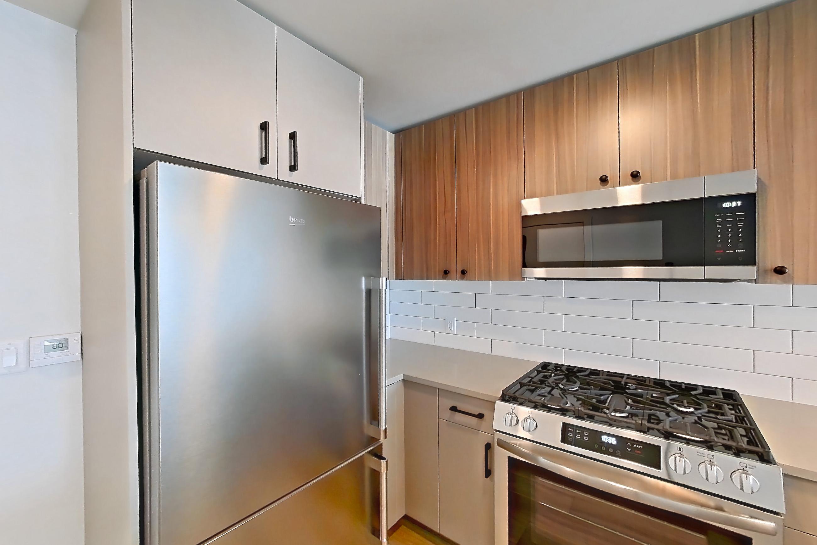 Kitchen with dishwasher, gas range, light countertops, light stone countertops, light wood-finish flooring, oven/range, refrigerator, and stainless steel appliances, Apartment 737 at The Myles