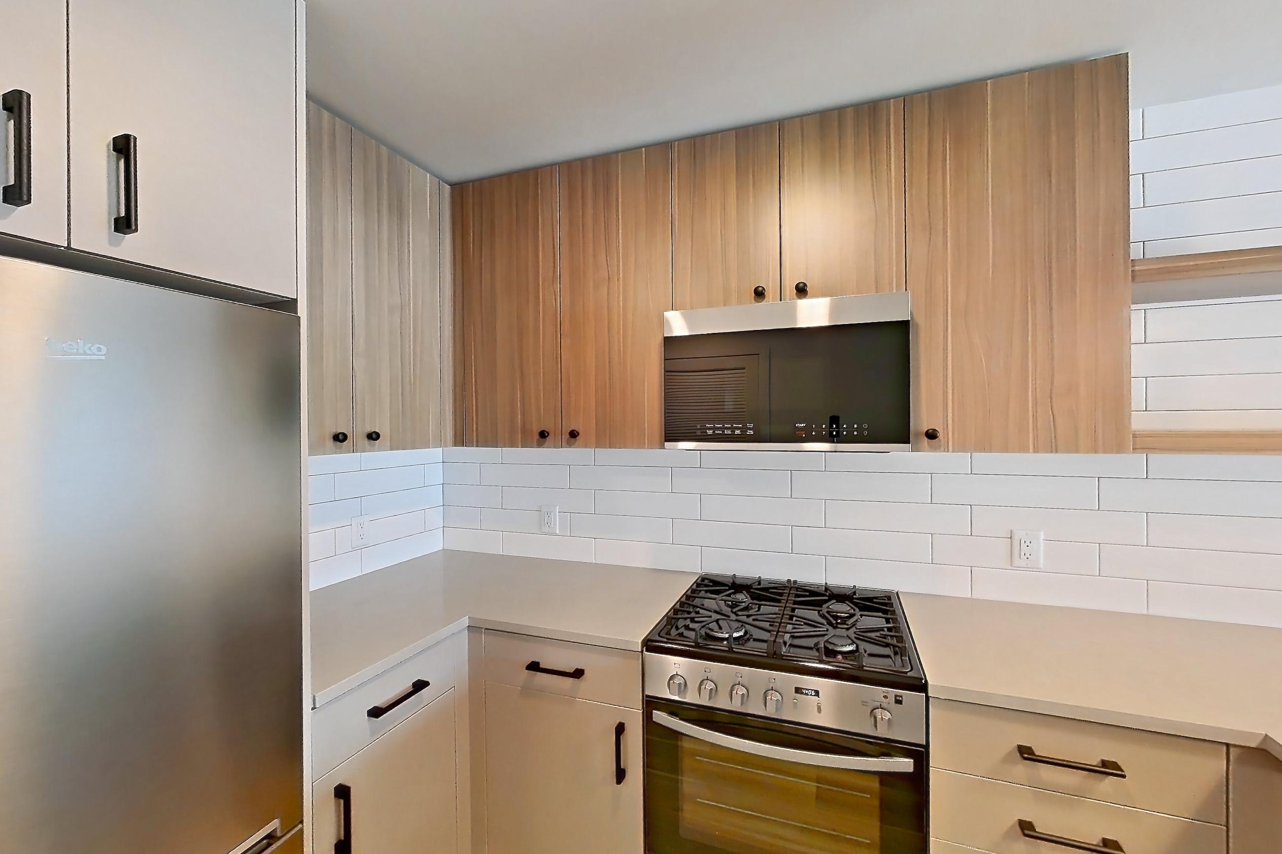 Kitchen with gas range, light countertops, light stone countertops, light wood-finish flooring, oven/range, refrigerator, and stainless steel appliances, Apartment 738 at The Myles
