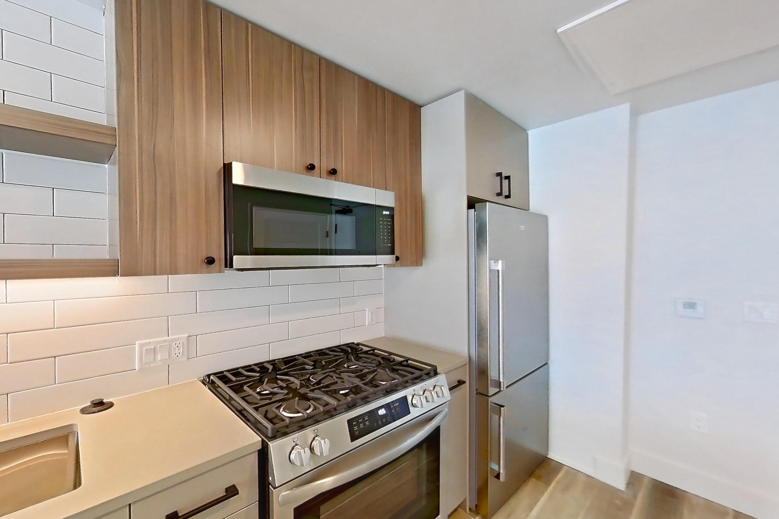 Kitchen with dishwasher, gas range, light countertops, light wood-finish flooring, oven/range, refrigerator, and stainless steel appliances, Apartment 741 at The Myles