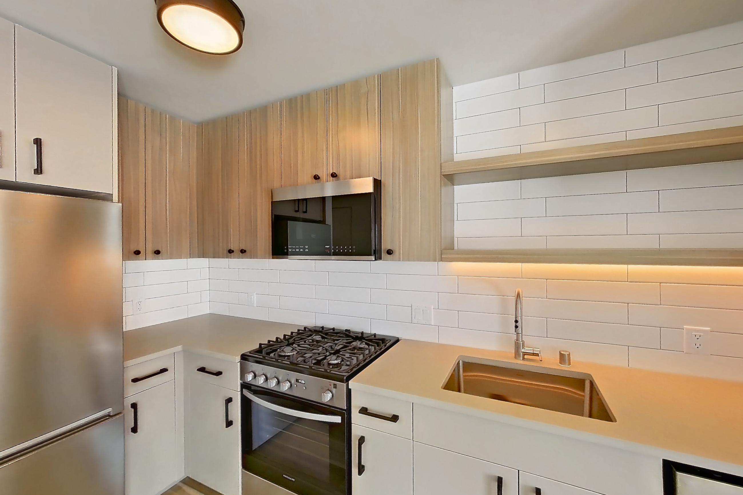 Kitchen with gas range, light countertops, light wood-finish flooring, oven/range, refrigerator, and stainless steel appliances, Apartment 745 at The Myles
