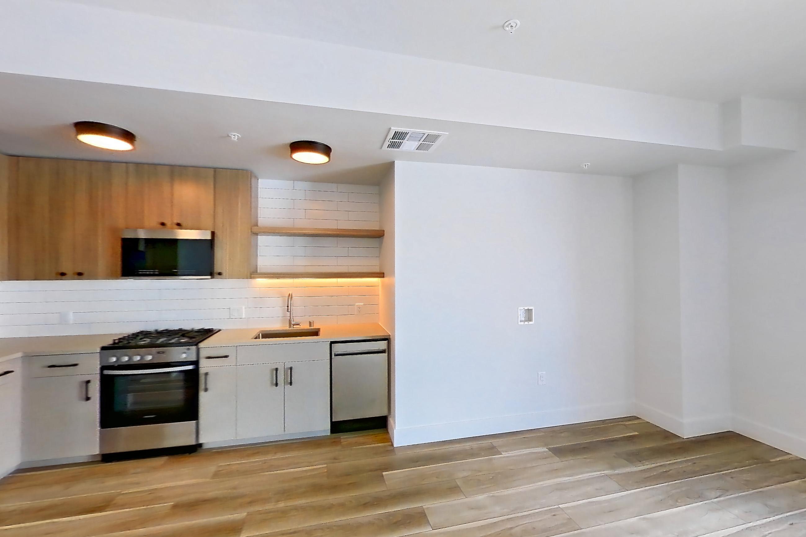 Living space with dishwasher, gas range, light countertops, light wood-finish flooring, microwave, oven/range, refrigerator, and stainless steel appliances, Apartment 745 at The Myles