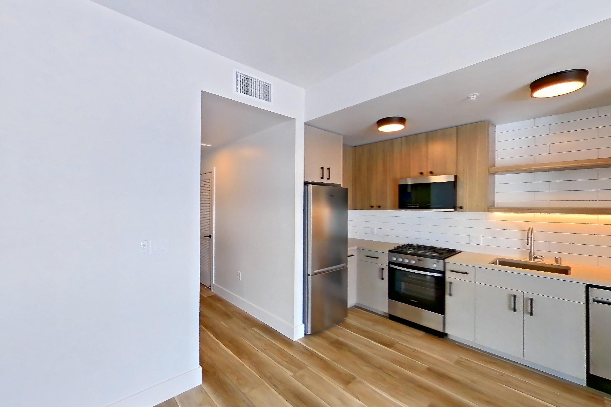 Living space with dishwasher, gas range, light countertops, light wood-finish flooring, microwave, oven/range, refrigerator, and stainless steel appliances, Apartment 745 at The Myles