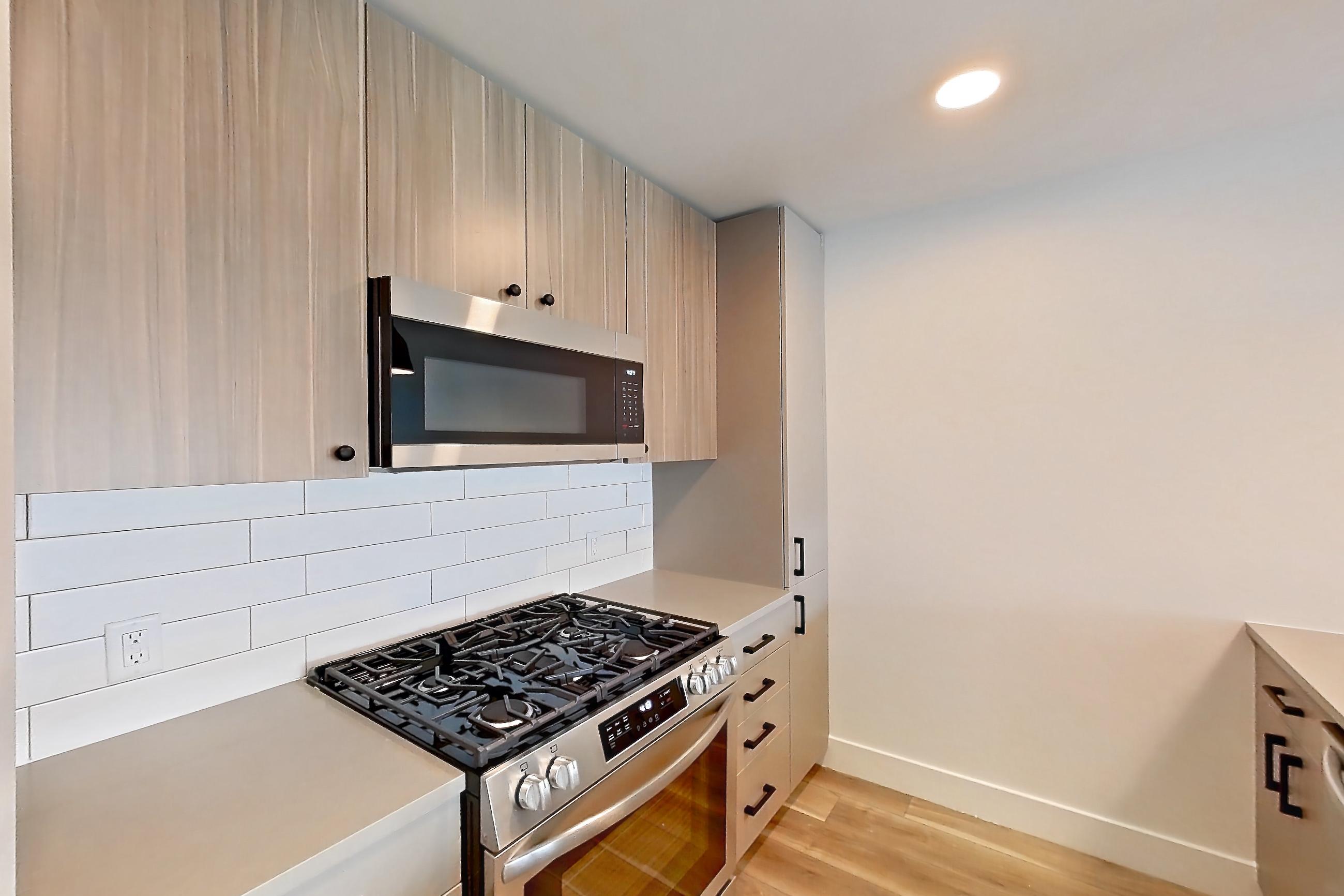 Kitchen with dishwasher, gas range, light countertops, light wood-finish flooring, microwave, oven/range, and stainless steel appliances, Apartment 746 at The Myles