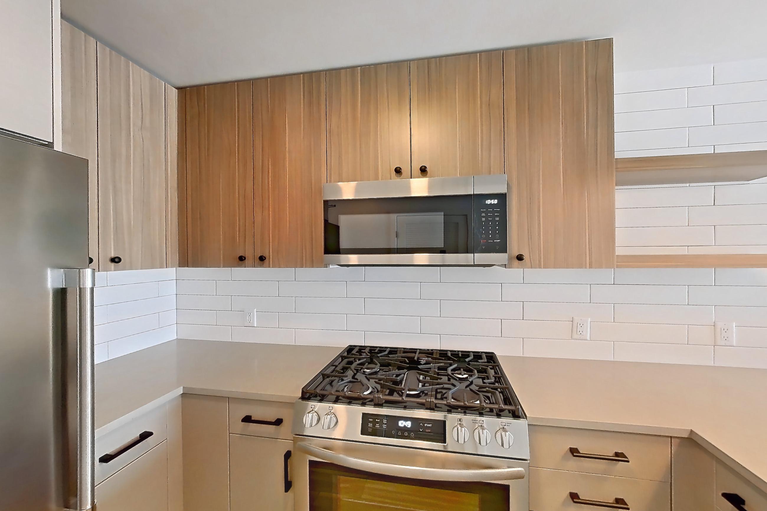 Kitchen with dishwasher, gas range, light countertops, light wood-finish flooring, microwave, oven/range, refrigerator, and stainless steel appliances, Apartment 747 at The Myles