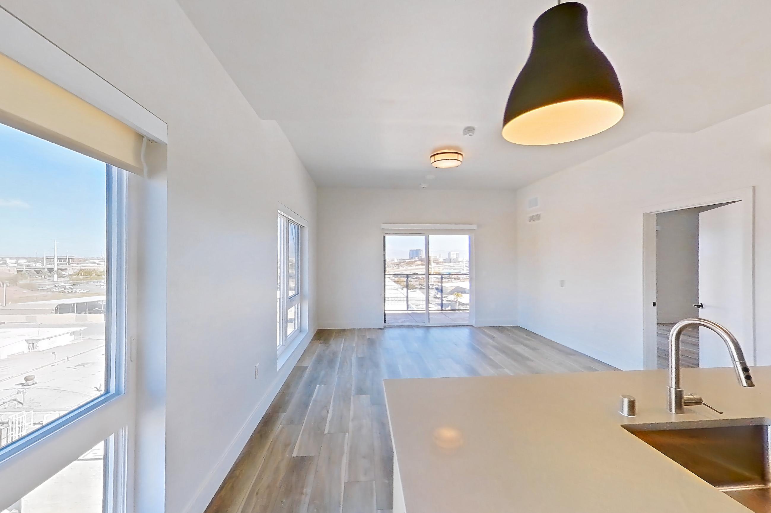 Kitchen with dark wood-finish flooring, dishwasher, gas range, kitchen island, light countertops, light stone countertops, light wood-finish flooring, oven/range, refrigerator, and stainless steel appliances, Apartment 749 at The Myles