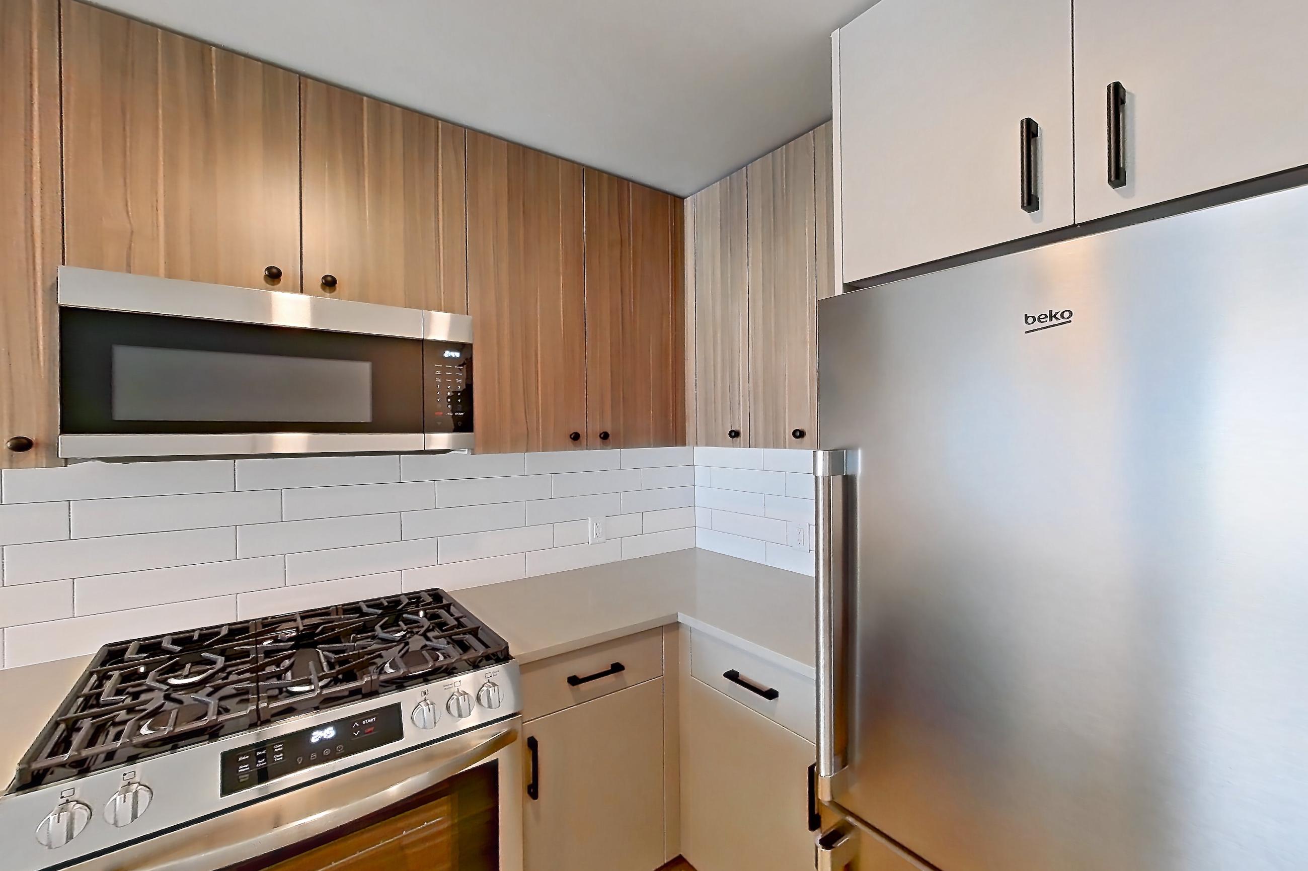 Kitchen with dishwasher, gas range, light countertops, light wood-finish flooring, oven/range, refrigerator, and stainless steel appliances, Apartment 750 at The Myles