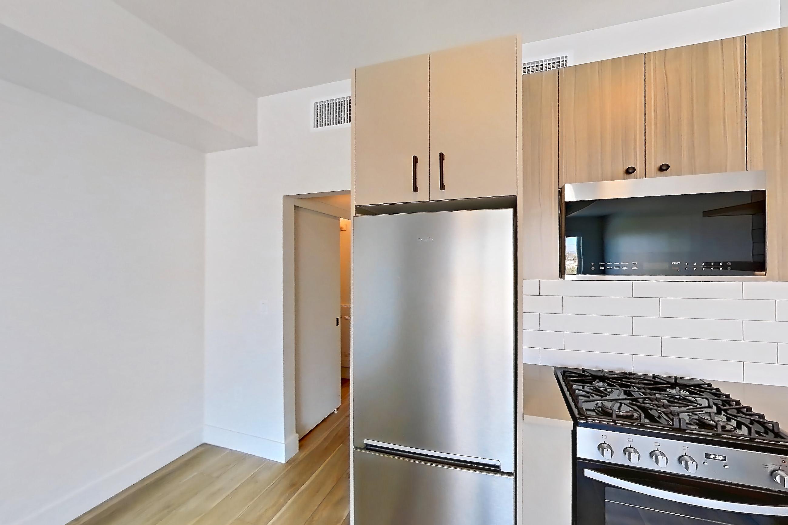 Kitchen with dishwasher, gas range, light countertops, light wood-finish flooring, oven/range, refrigerator, and stainless steel appliances, Apartment 751 at The Myles
