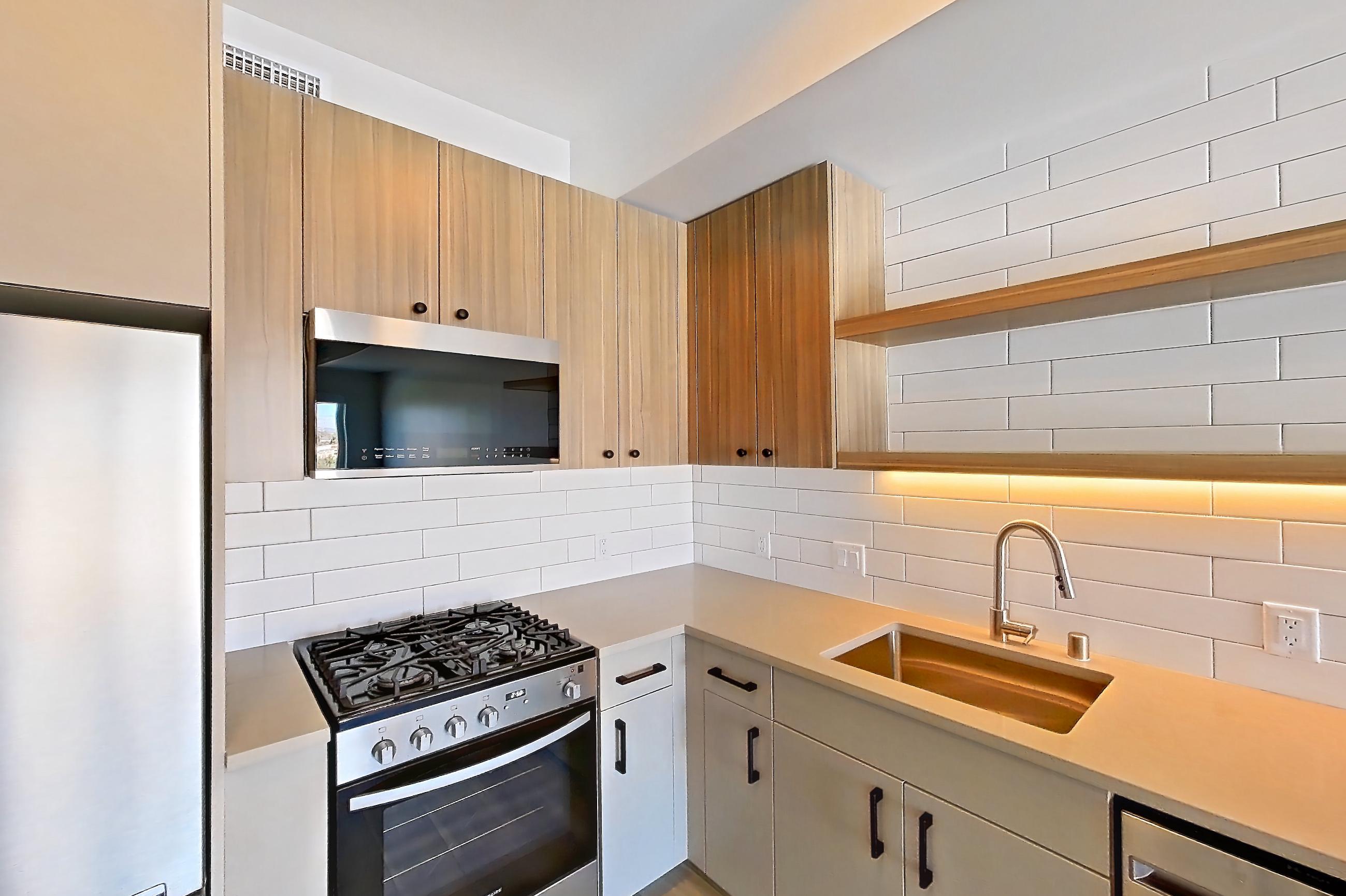 Kitchen with dishwasher, gas range, light countertops, light wood-finish flooring, oven/range, refrigerator, and stainless steel appliances, Apartment 751 at The Myles