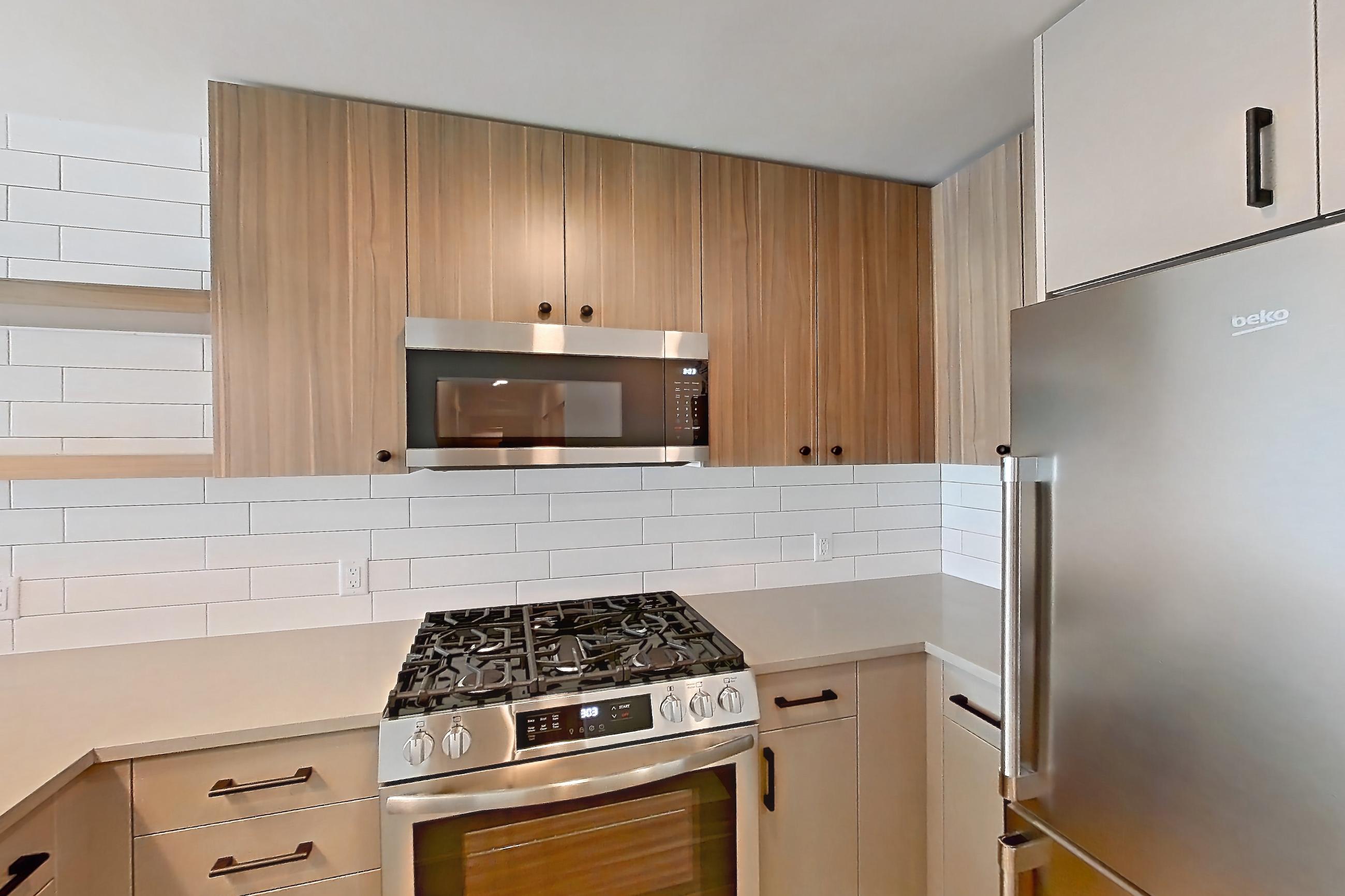 Kitchen with dishwasher, gas range, light countertops, light wood-finish flooring, microwave, oven/range, refrigerator, and stainless steel appliances, Apartment 752 at The Myles