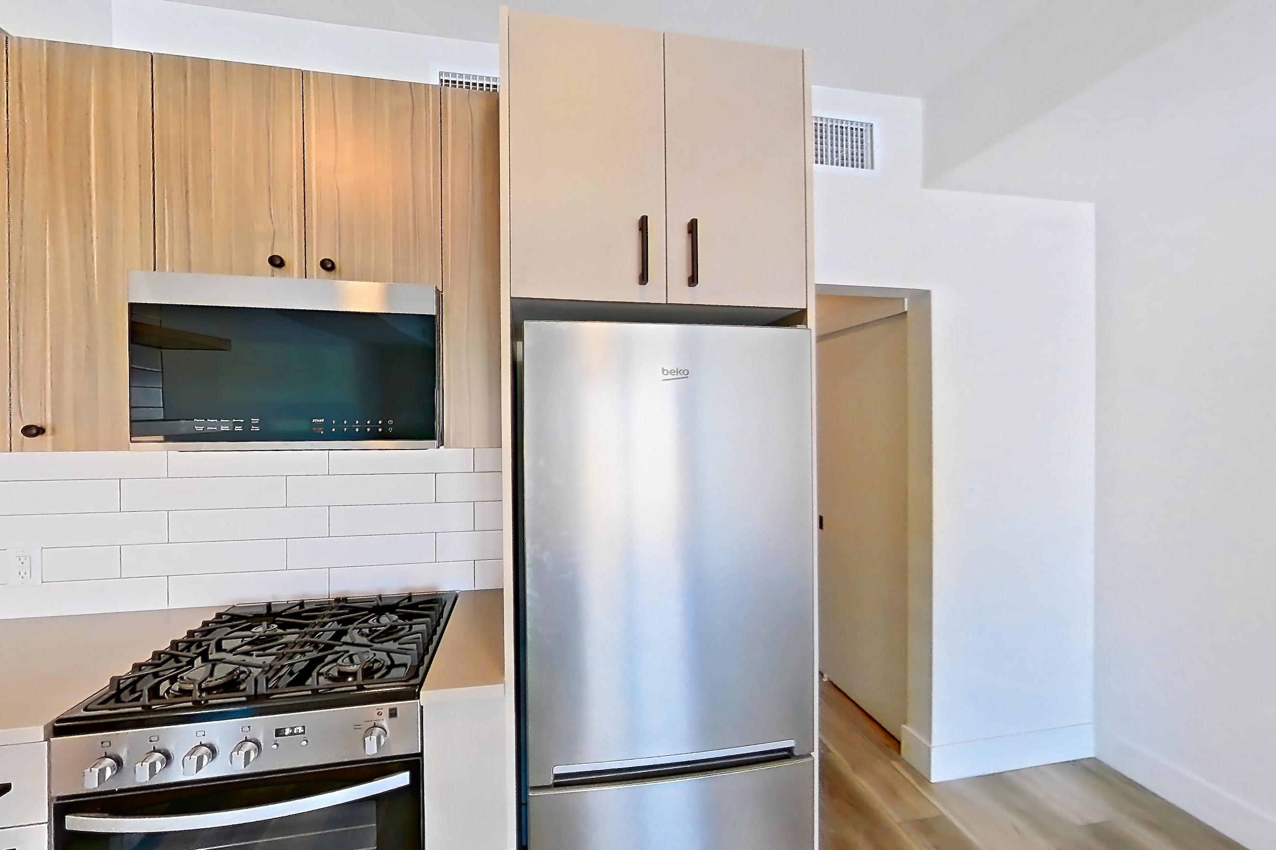 Kitchen with dishwasher, gas range, light countertops, light wood-finish flooring, oven/range, refrigerator, and stainless steel appliances, Apartment 753 at The Myles