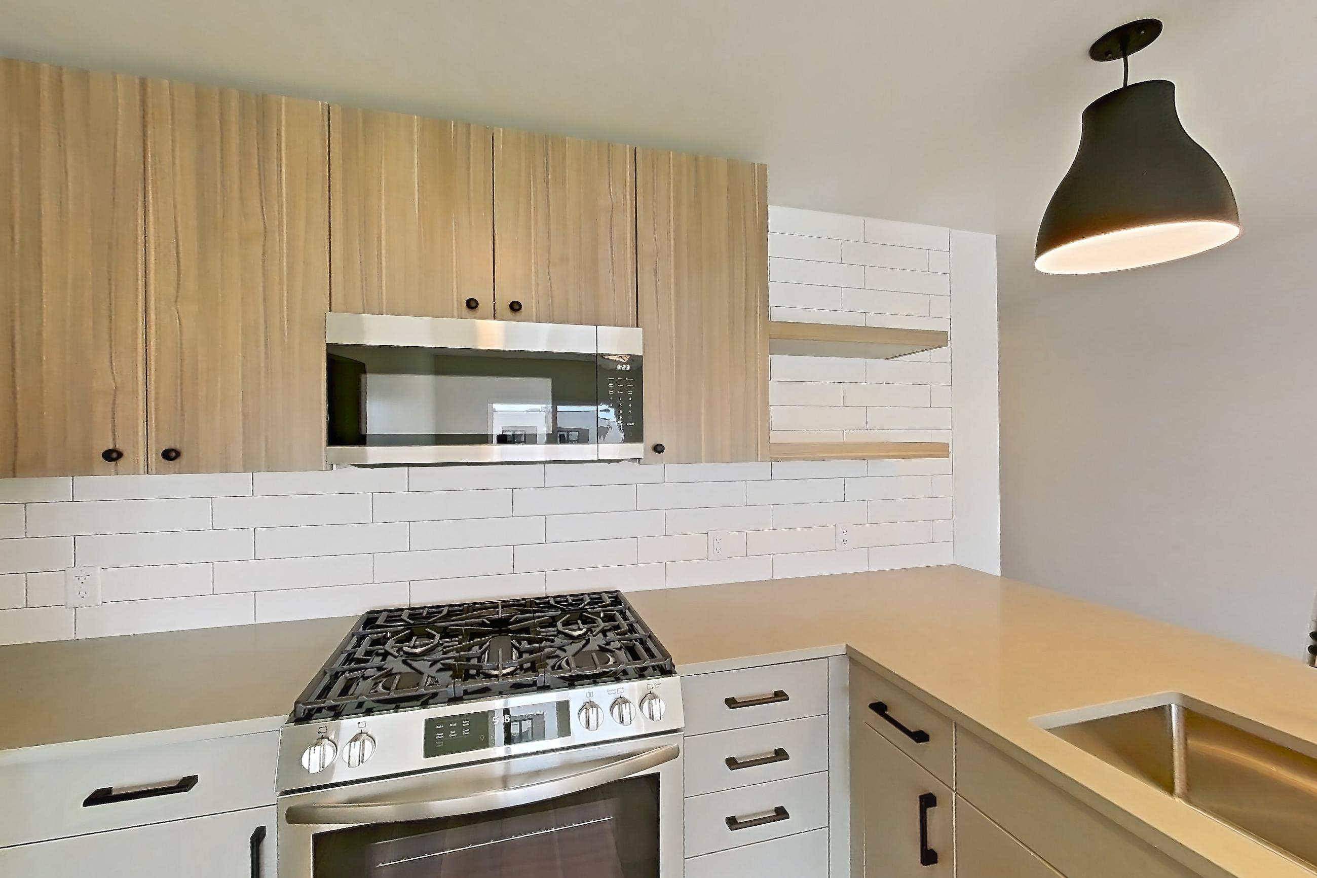 Kitchen with dishwasher, gas range, light countertops, light wood-finish flooring, microwave, oven/range, refrigerator, and stainless steel appliances, Apartment 754 at The Myles