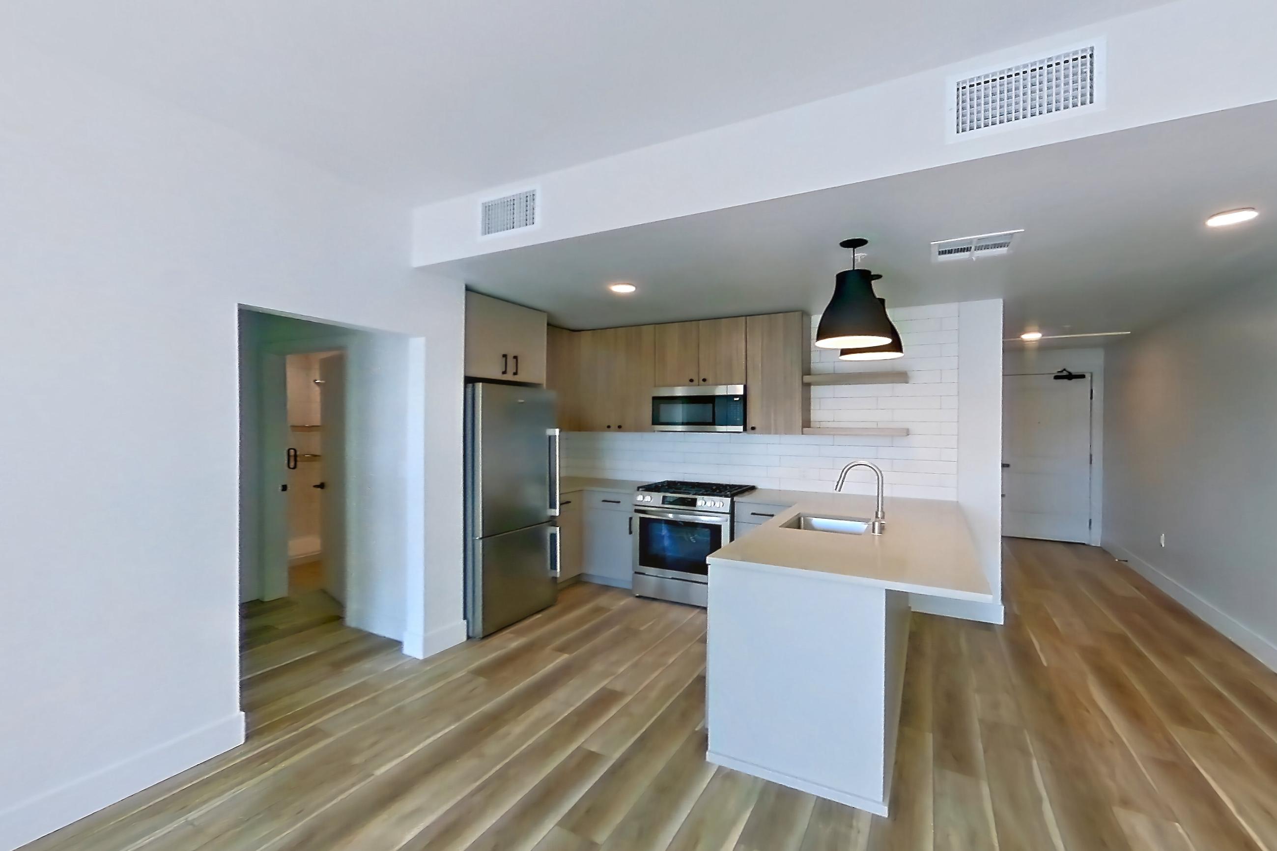 Living room with gas range, light countertops, light wood-finish flooring, oven/range, range hood, refrigerator, and stainless steel appliances, Apartment 754 at The Myles