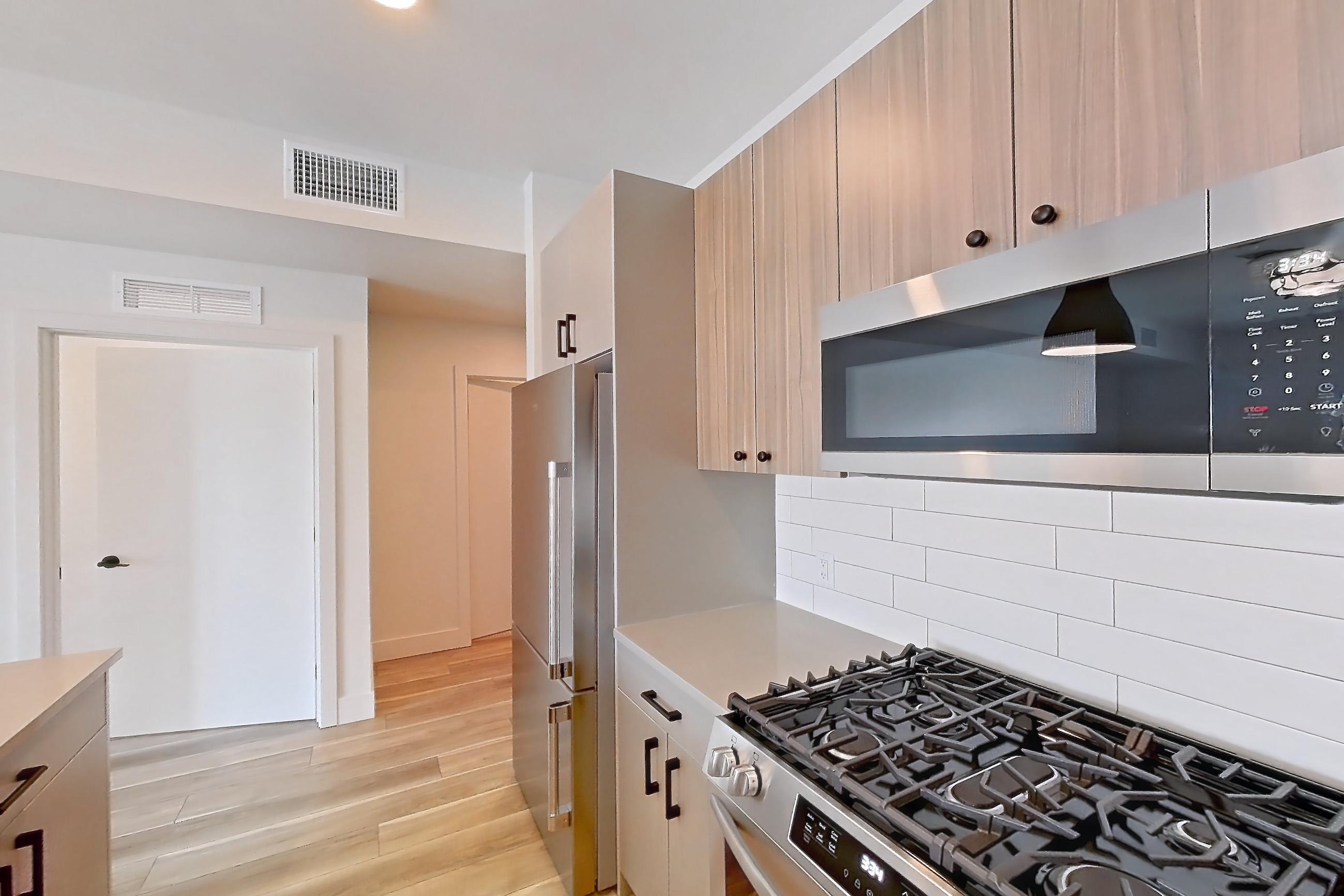Kitchen with dishwasher, gas range, light countertops, light wood-finish flooring, oven/range, refrigerator, and stainless steel appliances, Apartment 755 at The Myles