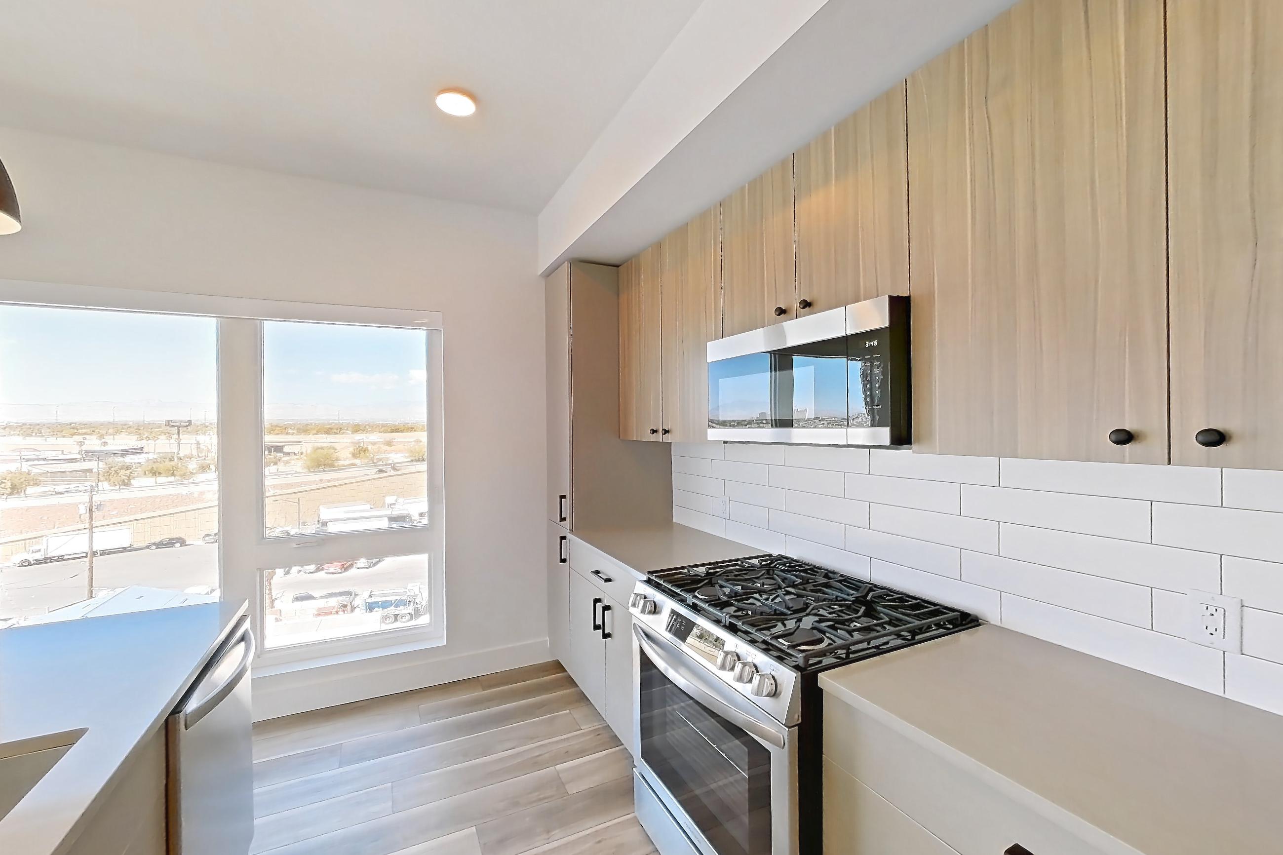 Kitchen with gas range, kitchen island, light countertops, light stone countertops, light wood-finish flooring, oven/range, and stainless steel appliances, Apartment 758 at The Myles