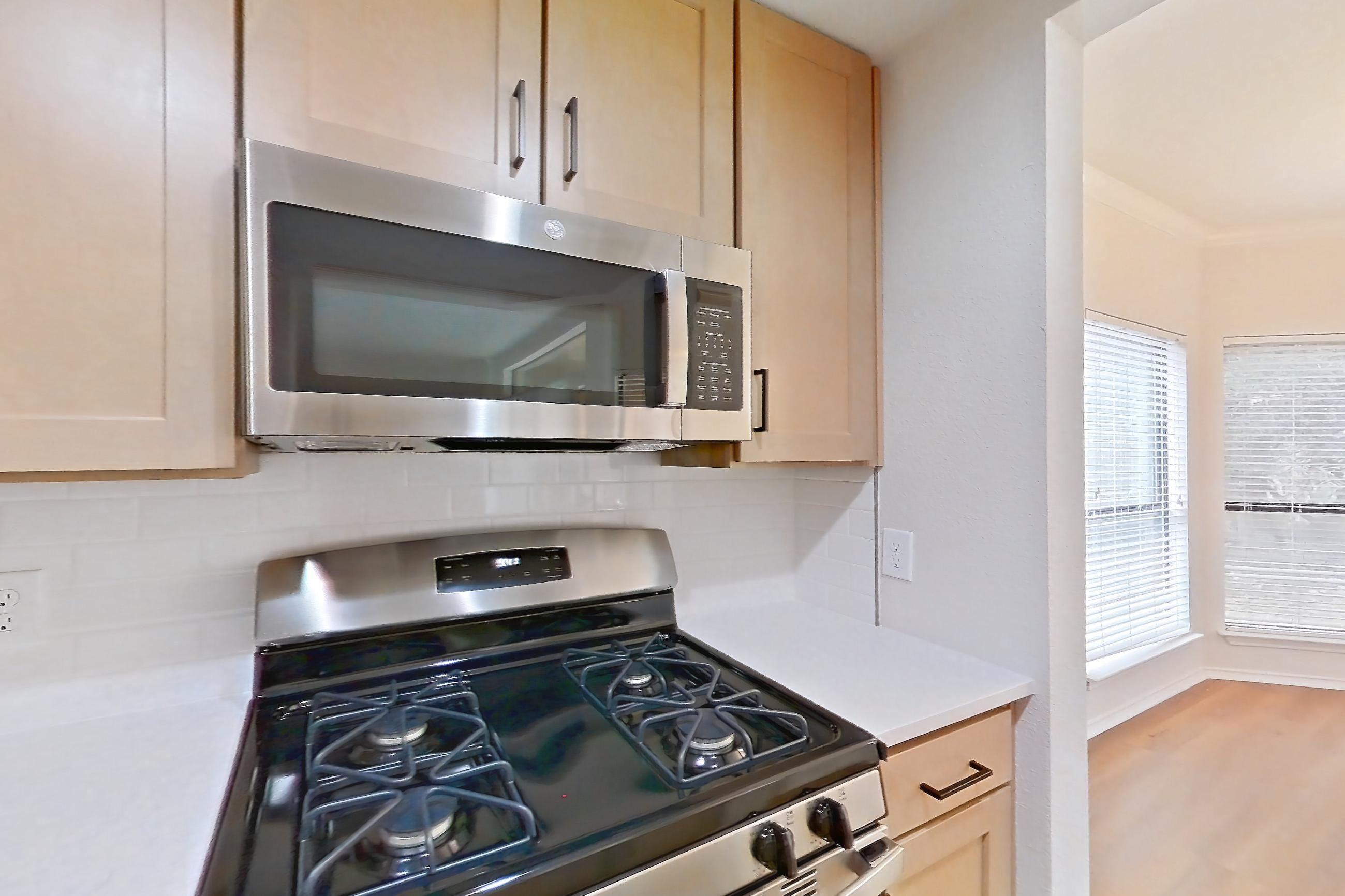 Kitchen with dishwasher, gas range, light countertops, light stone countertops, light wood-finish flooring, microwave, oven/range, and stainless steel appliances, Apartment 2001 at Marquis at Caprock Canyon