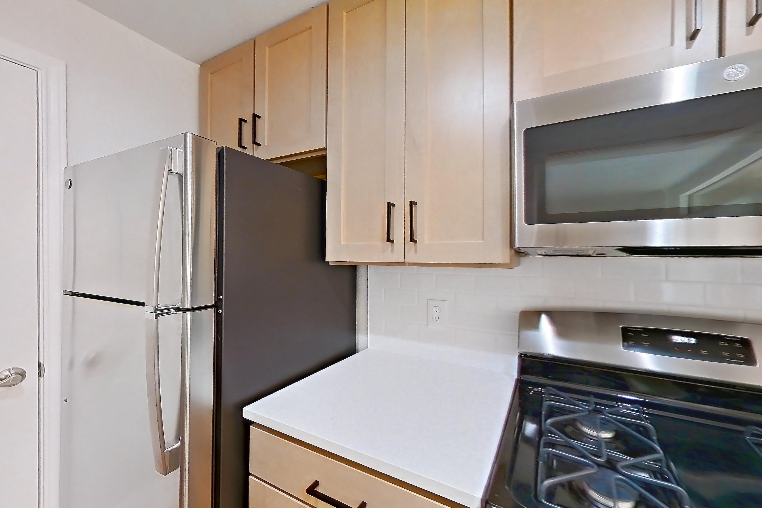 Kitchen with dishwasher, gas range, light countertops, light stone countertops, light wood-finish flooring, microwave, oven/range, and stainless steel appliances, Apartment 2001 at Marquis at Caprock Canyon