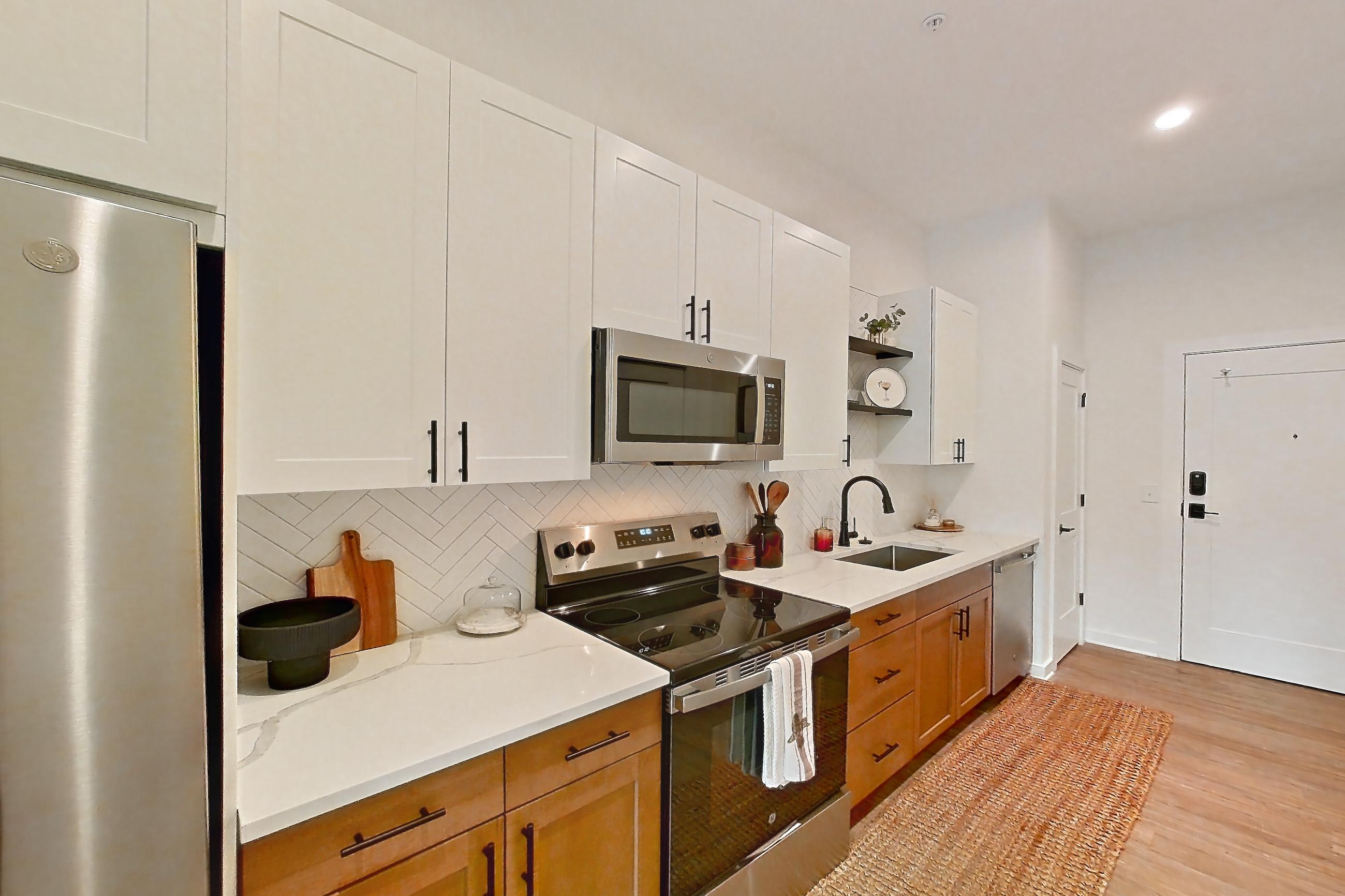 Kitchen with electric range, light countertops, light stone countertops, light wood-finish flooring, microwave, oven/range, refrigerator, and stainless steel appliances, Apartment 334 at The Rowe at Commonwealth