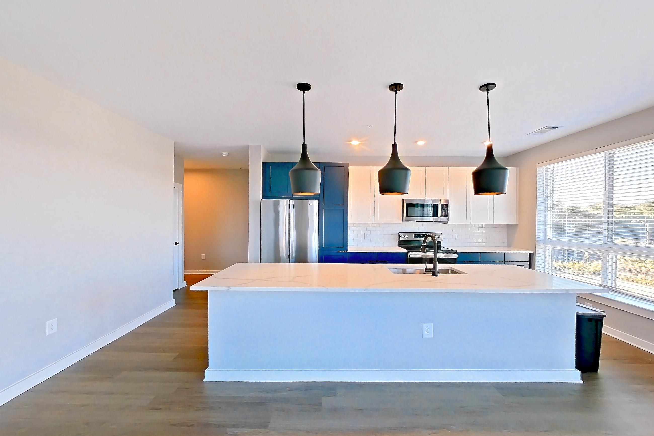 Living space with dark wood-finish flooring, electric range, kitchen island, light countertops, light stone countertops, oven/range, refrigerator, and stainless steel appliances, Apartment 615 at The Rowe at Commonwealth