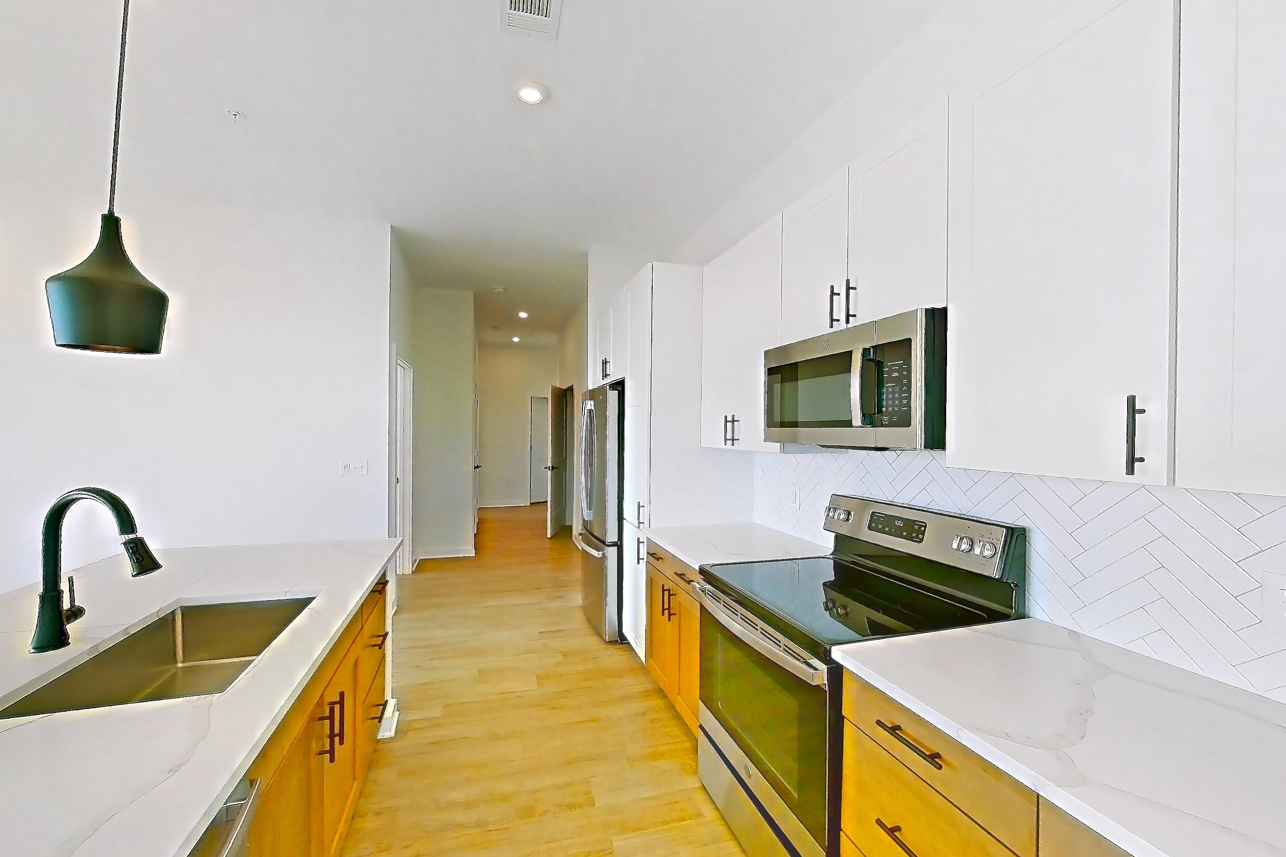 Kitchen with electric range, kitchen island, light countertops, light stone countertops, light wood-finish flooring, microwave, oven/range, refrigerator, and stainless steel appliances, Apartment 758 at The Rowe at Commonwealth